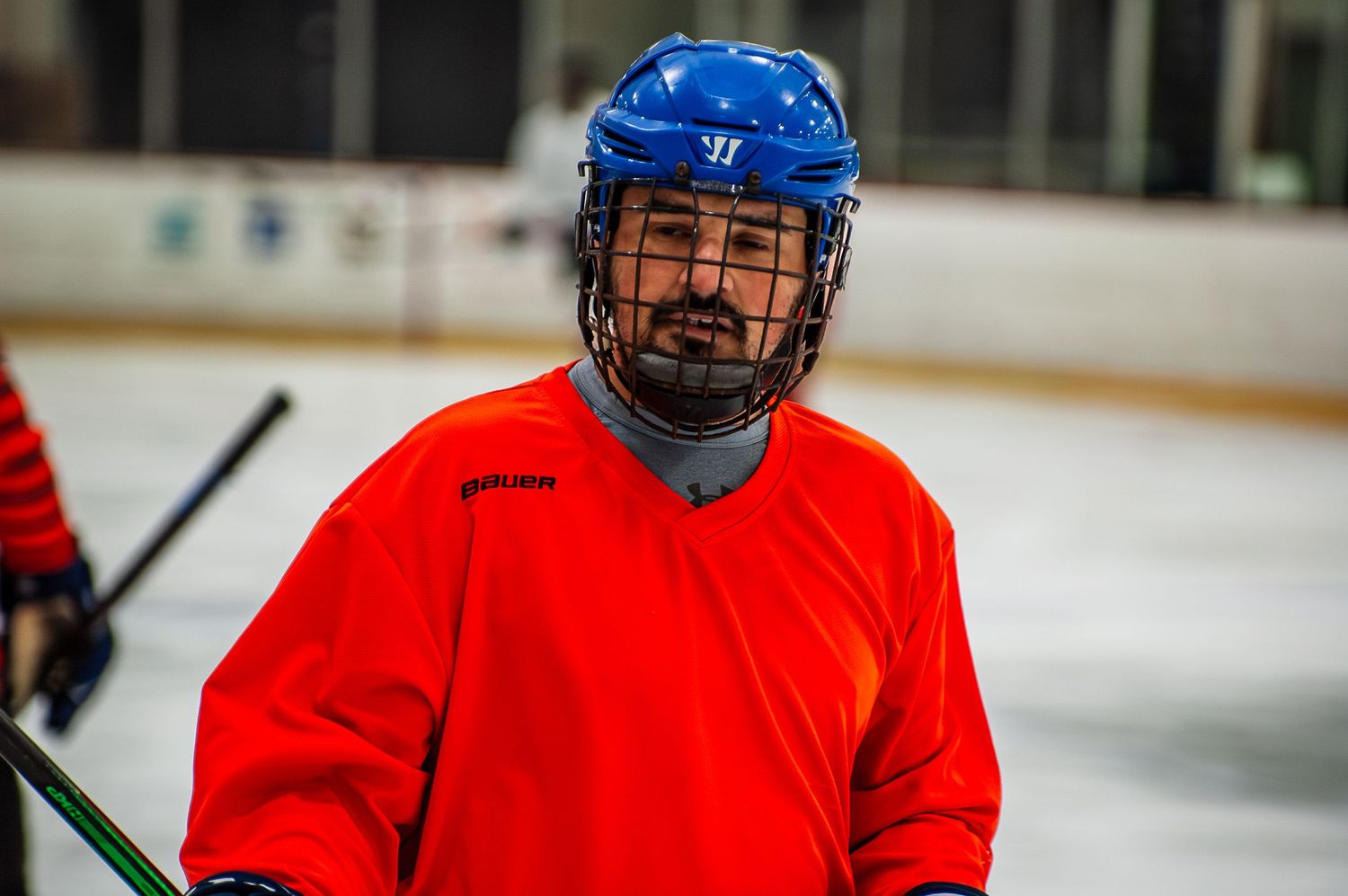Male hockey player in red jersey and blue Warrior helmet smiling on ice rink.