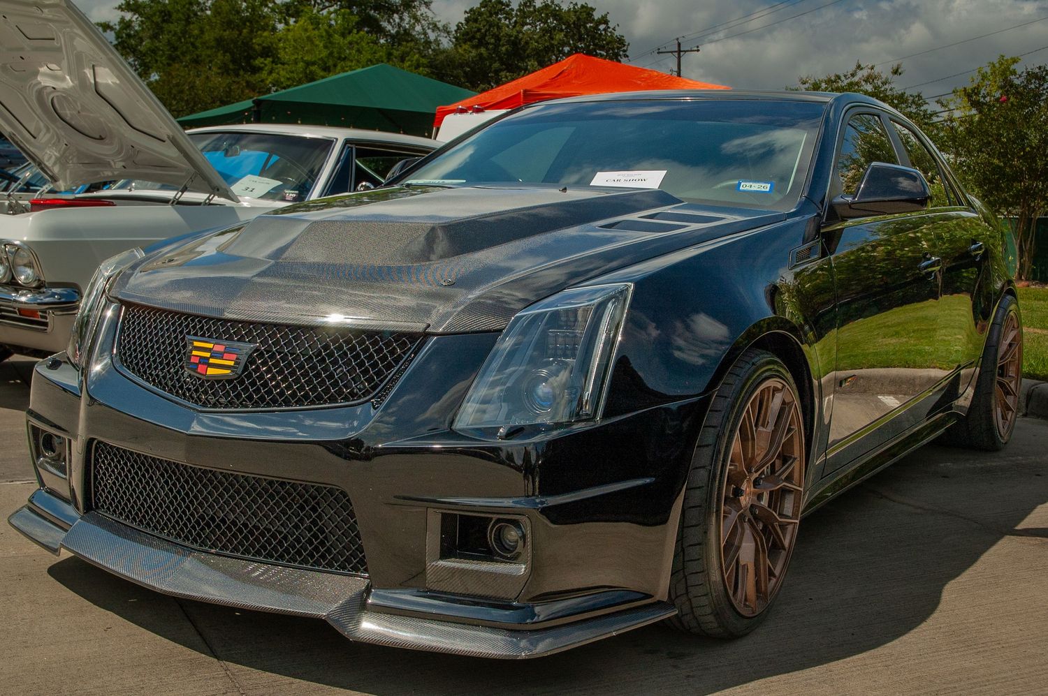 Black Cadillac CTS-V with bronze wheels and aggressive body kit on display at an outdoor car show.