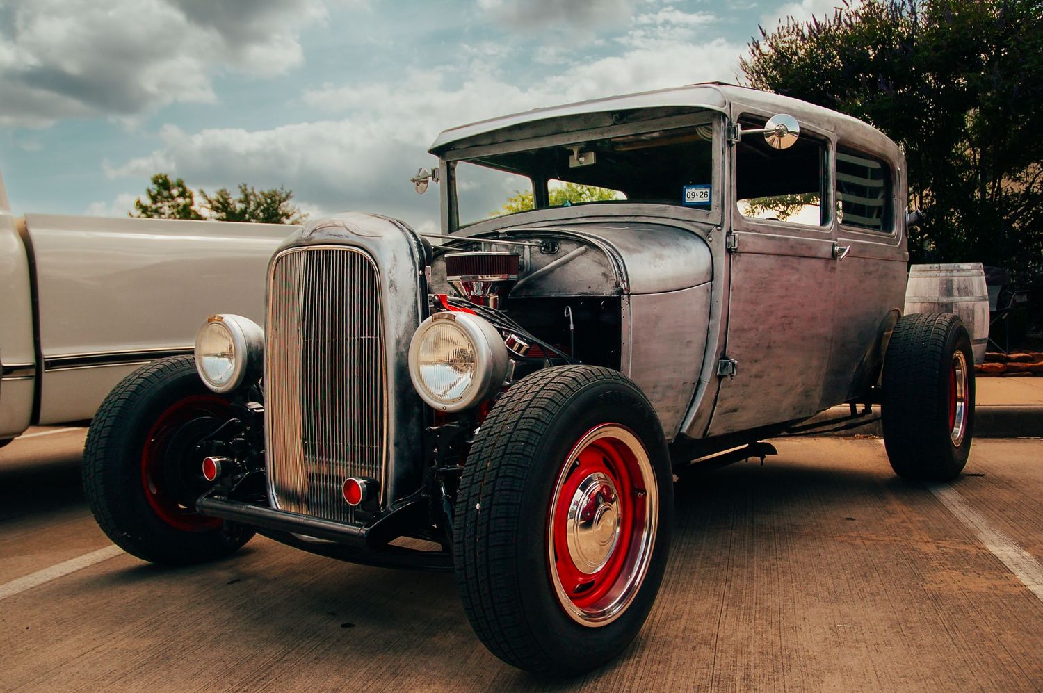 Rustic rat rod hot rod with exposed engine and red wheels parked at an outdoor car show.