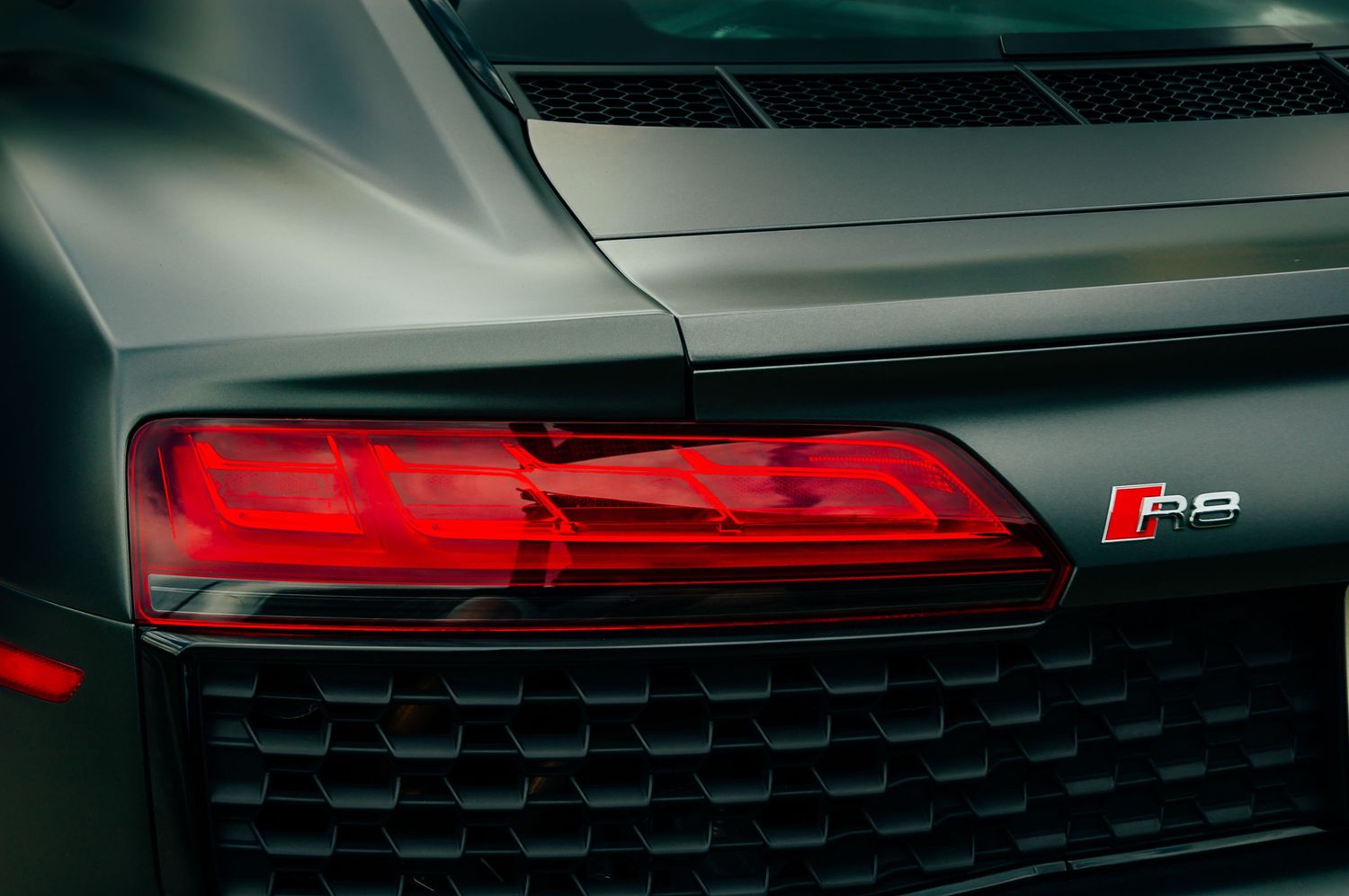 Close-up of red LED taillight and R8 badge on matte gray Audi R8 supercar.