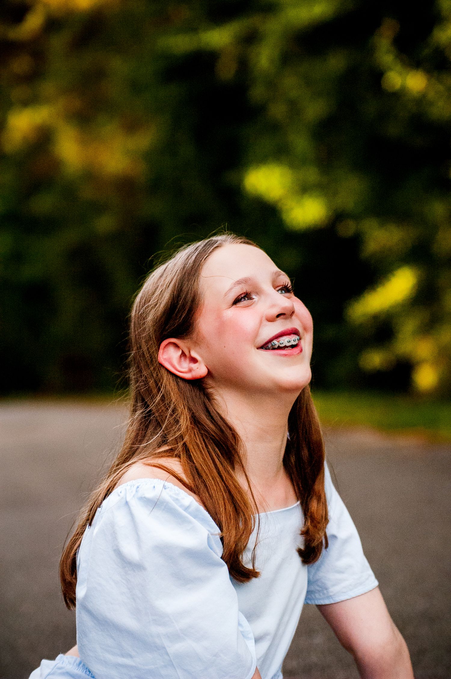 Laughing teenage girl with braces and brown hair wearing a light blue top outdoors.