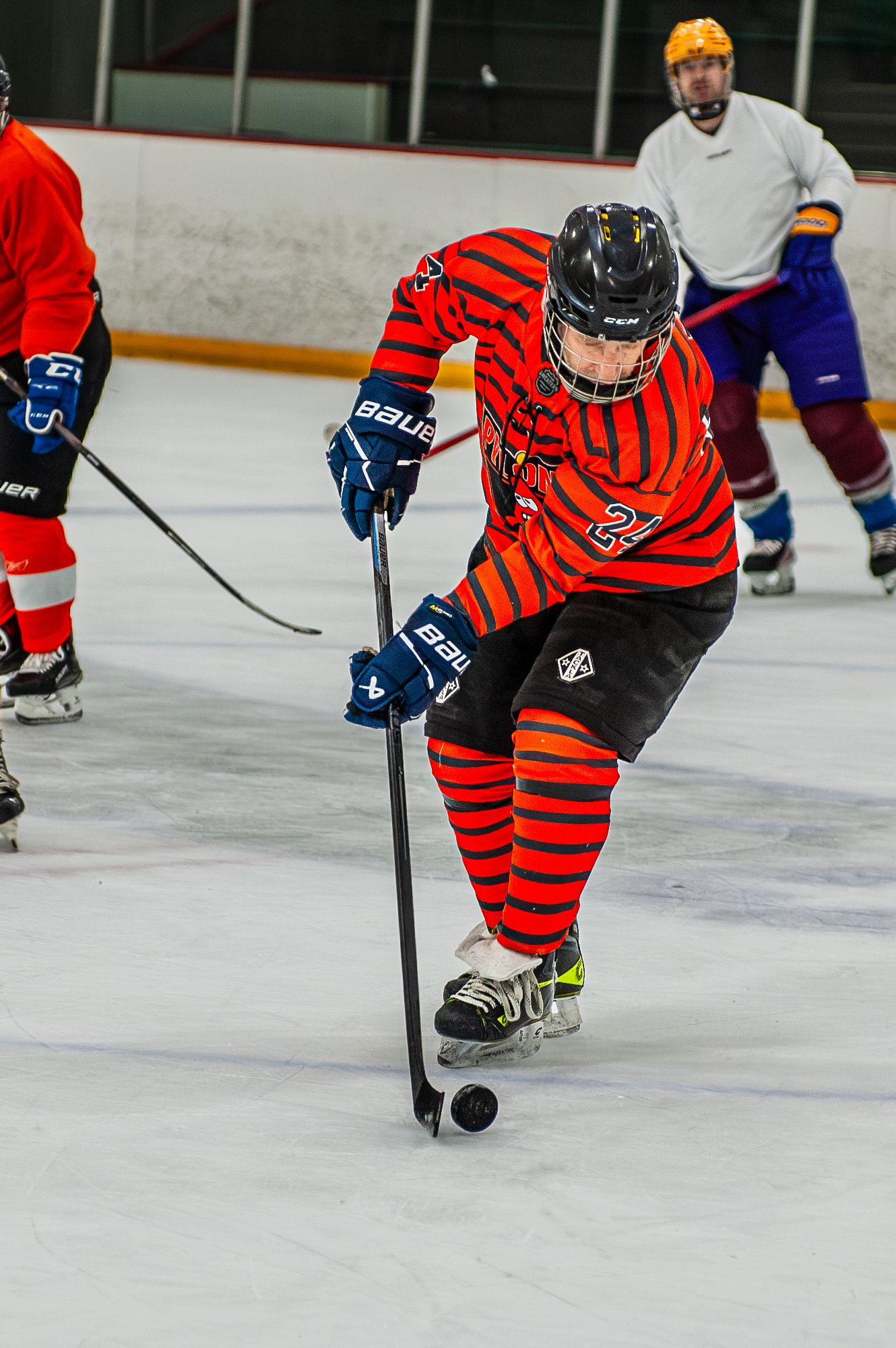 Hockey player in red striped jersey controlling puck during competitive ice hockey game.