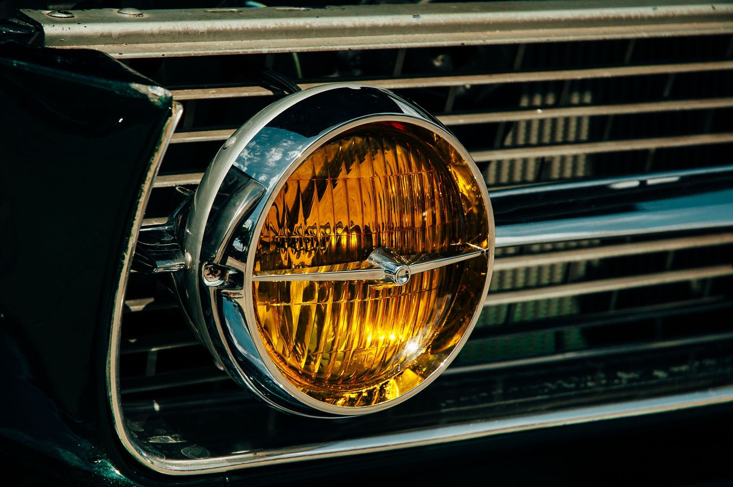 Vintage amber round headlight with chrome trim on classic black muscle car grille.
