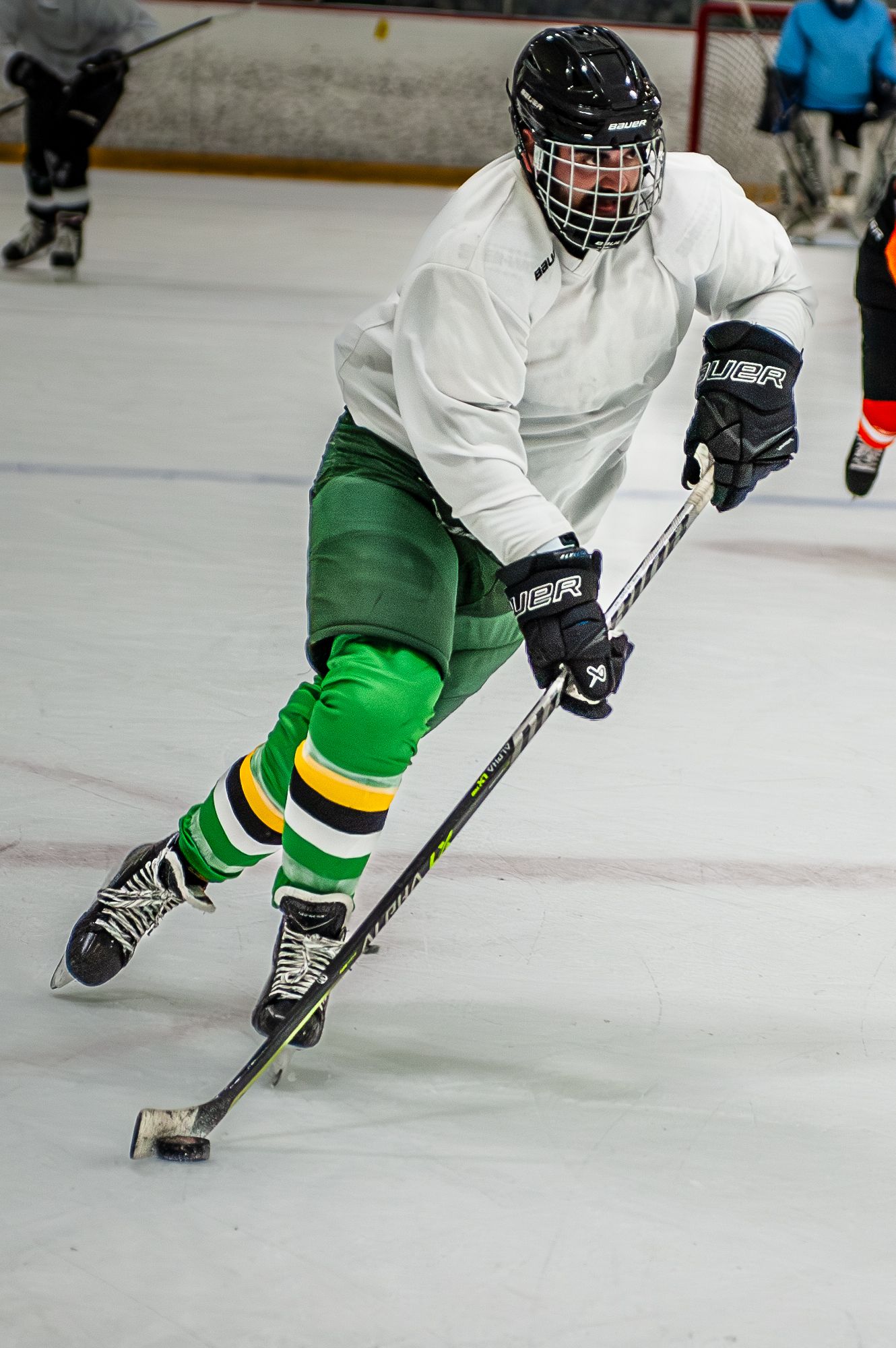 Young hockey player in green pants and white jersey controlling puck on ice.