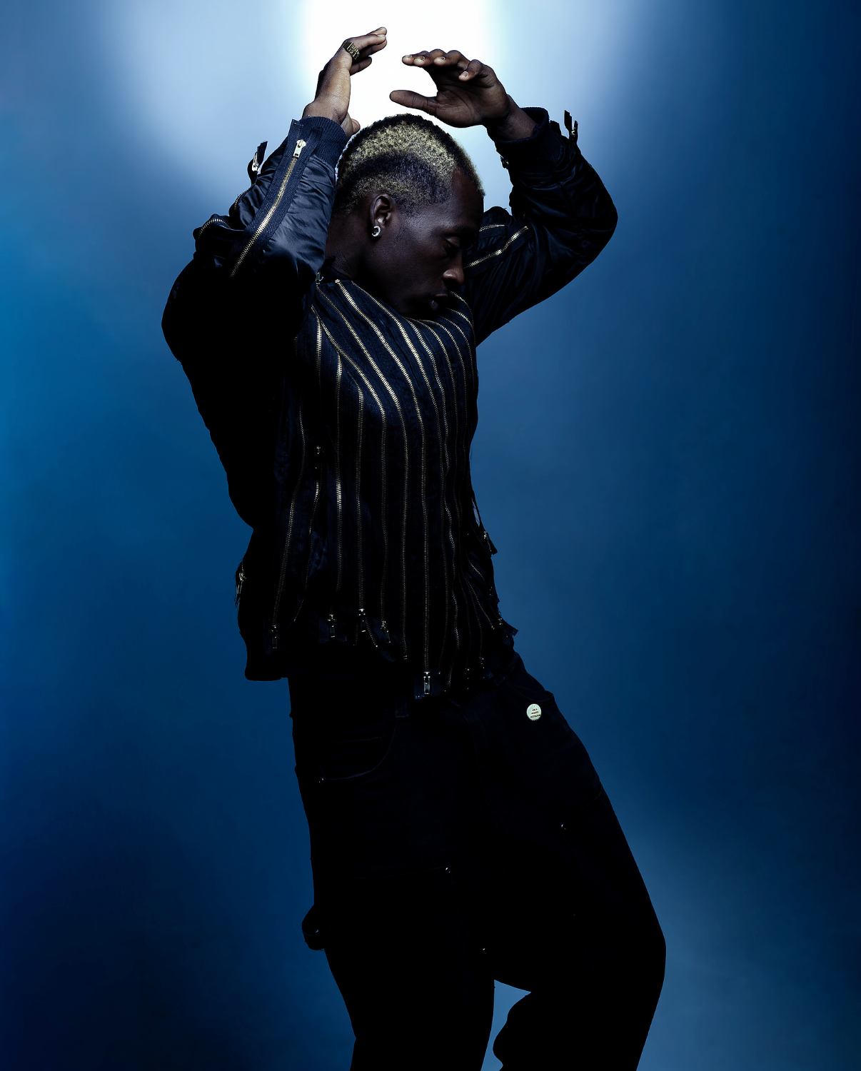 Boy in blue, moody lighting, hands over his head wearing a street style bomber jacket