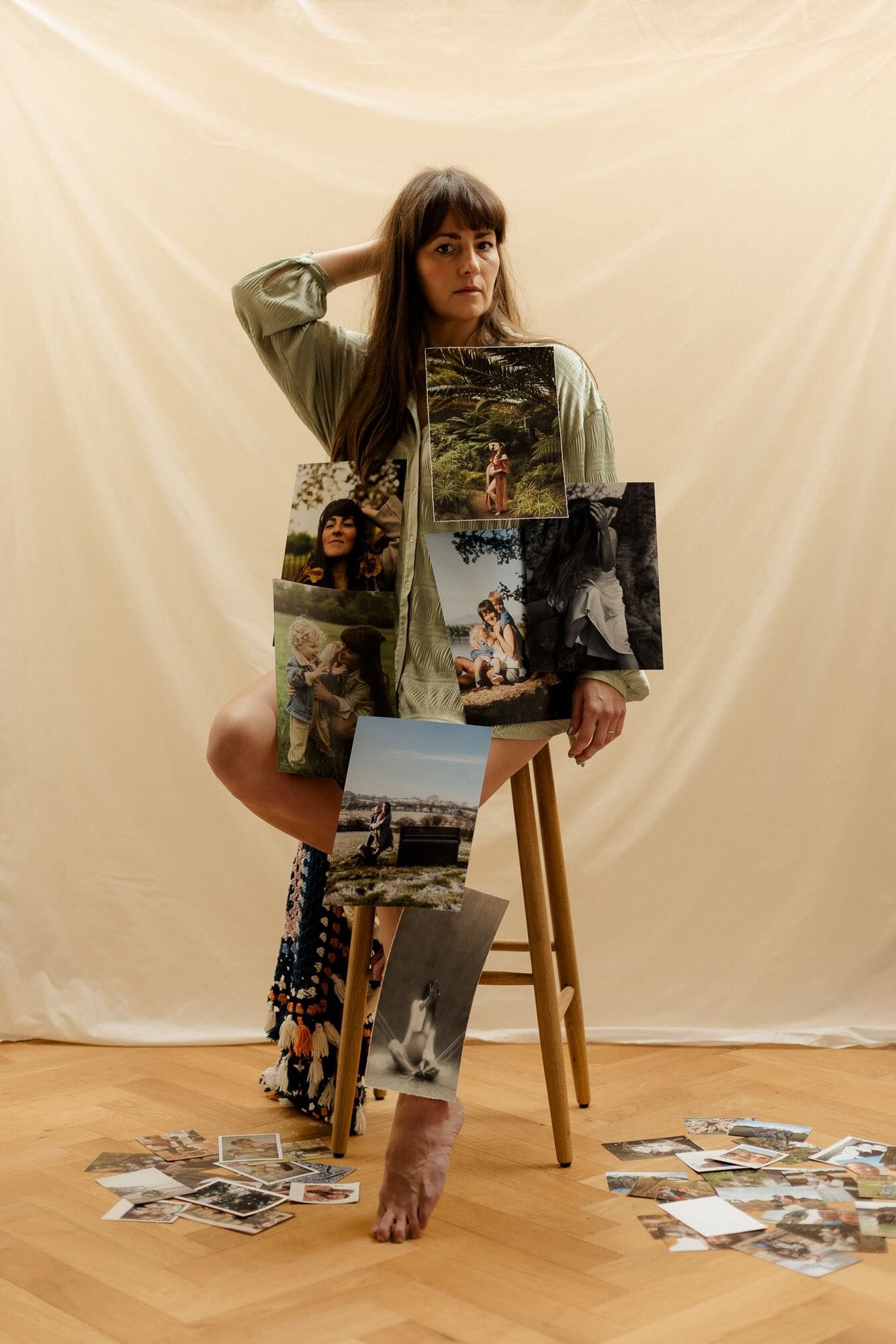 Woman sitting on a stool covered in printed photographs against a cream fabric backdrop.