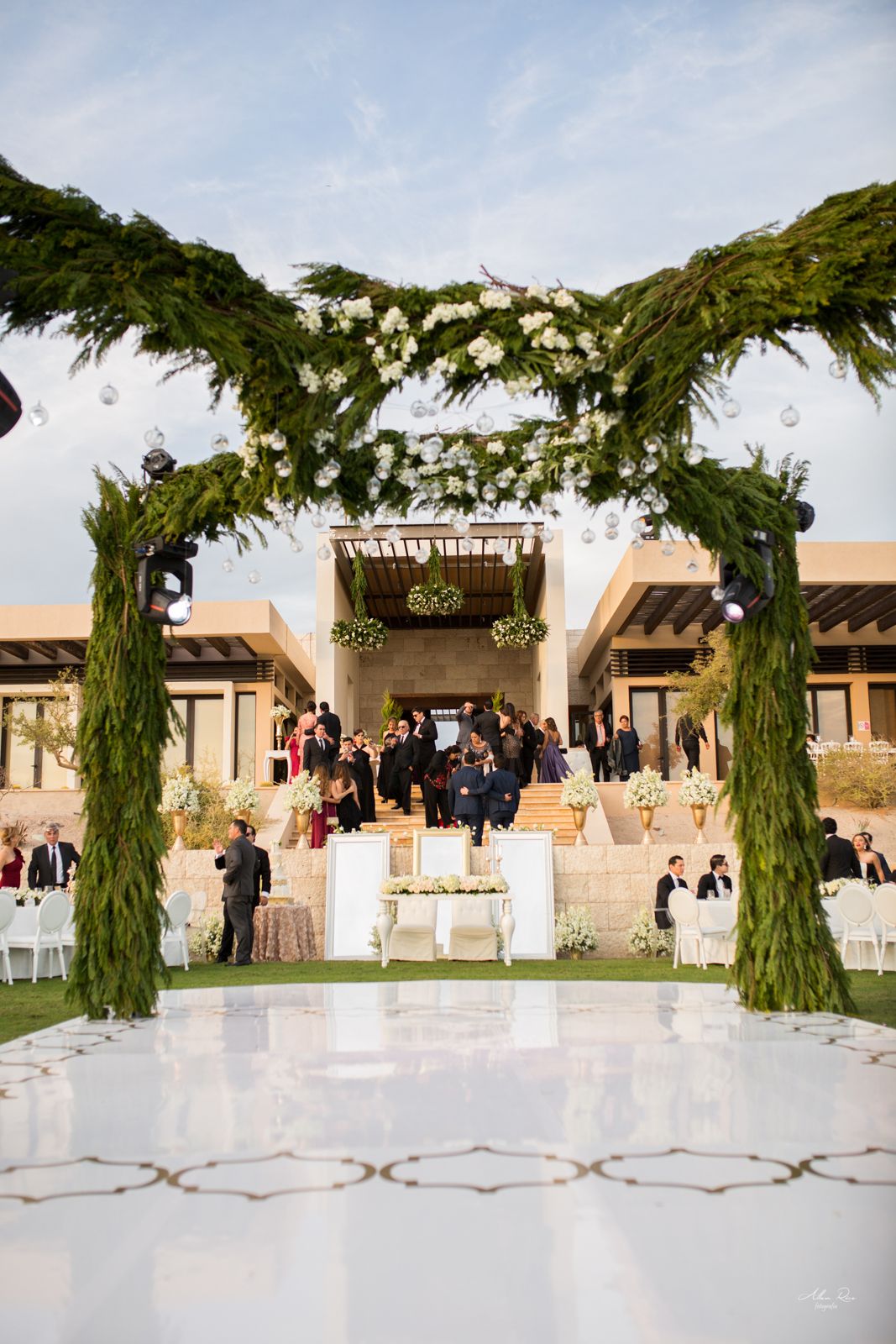 Grand outdoor wedding ceremony venue with lush green floral arches framing a white dance floor.