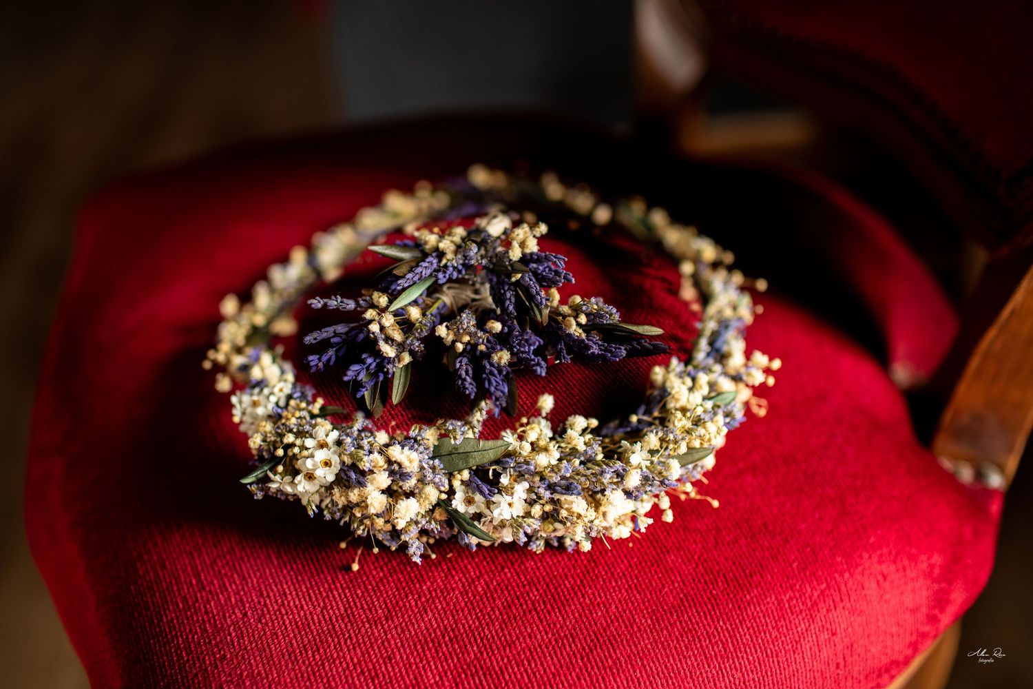Decorative floral wedding crown with dried purple flowers and baby's breath on red velvet chair.