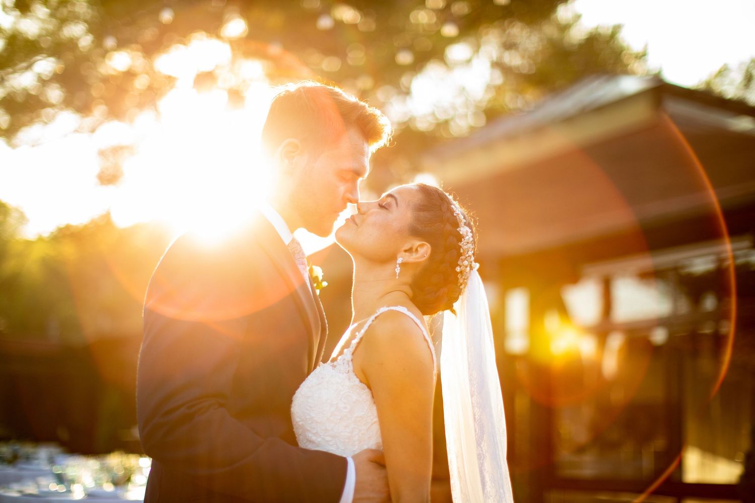 Bride and groom sharing romantic embrace bathed in stunning golden sunset lens flare outdoors.