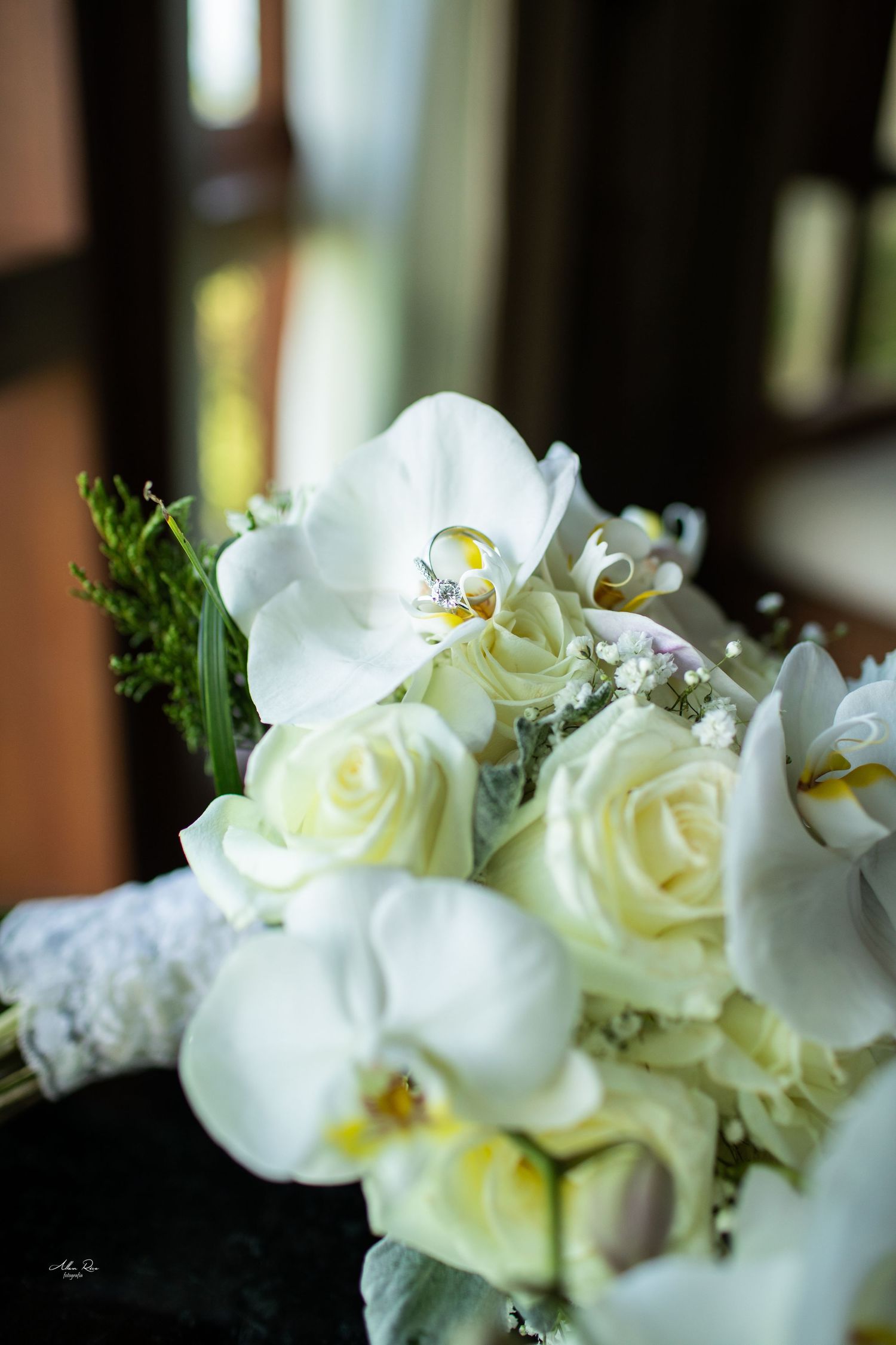 Wedding rings rest delicately on a bouquet of white orchids and cream roses.
