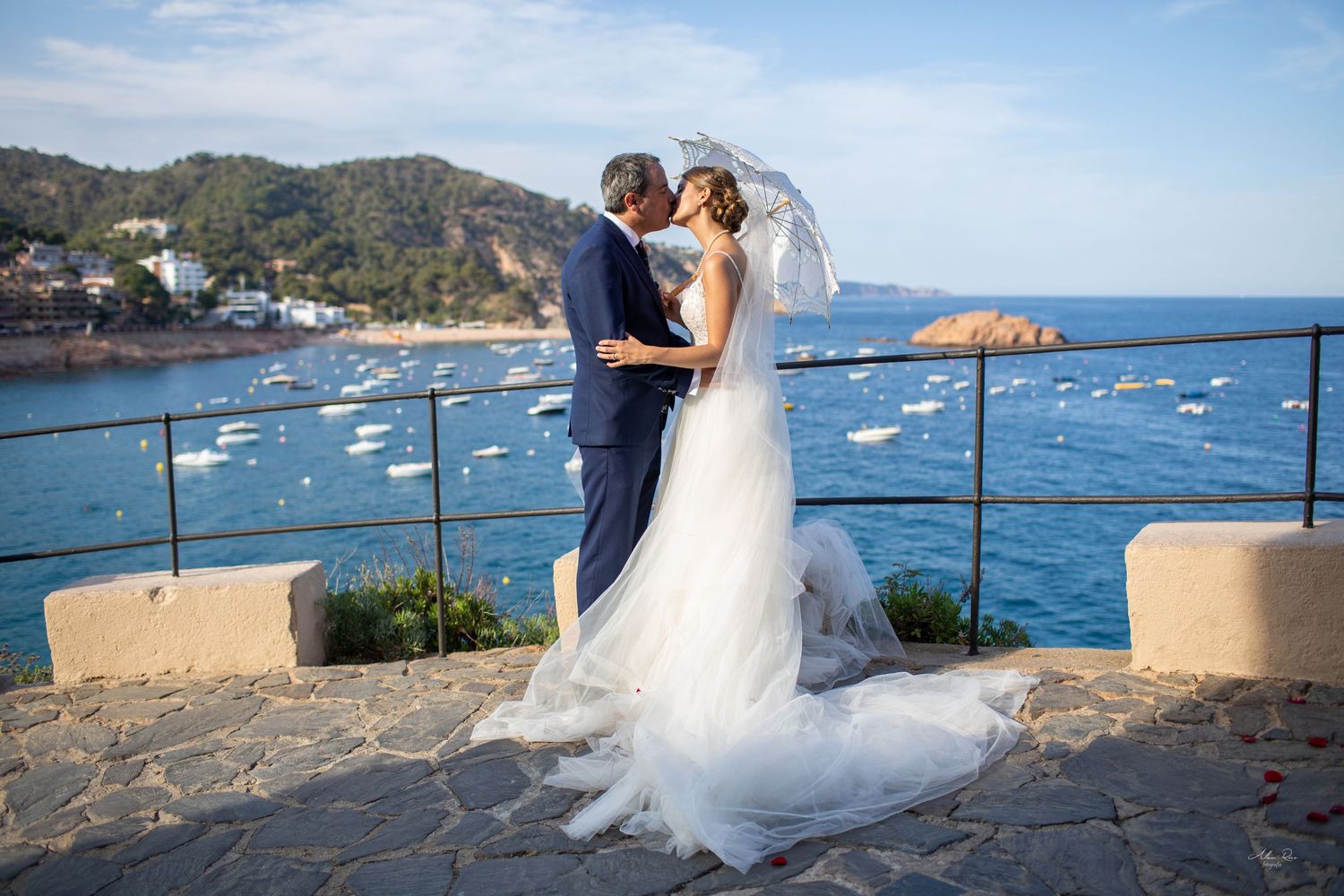 Bride and groom share a romantic kiss overlooking a beautiful Mediterranean coastal bay at golden hour.