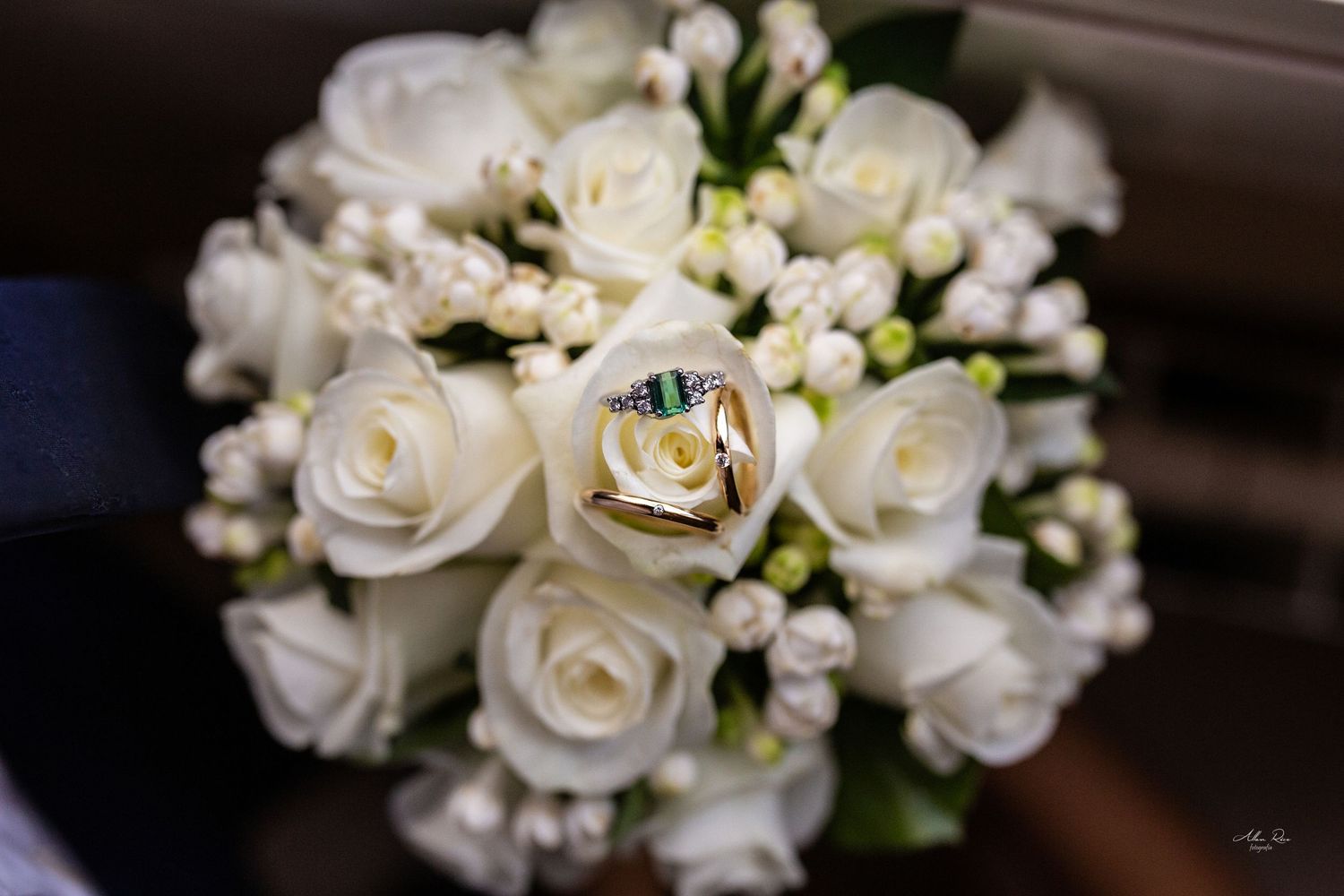 White rose wedding bouquet with gold heart-shaped rings resting on top.
