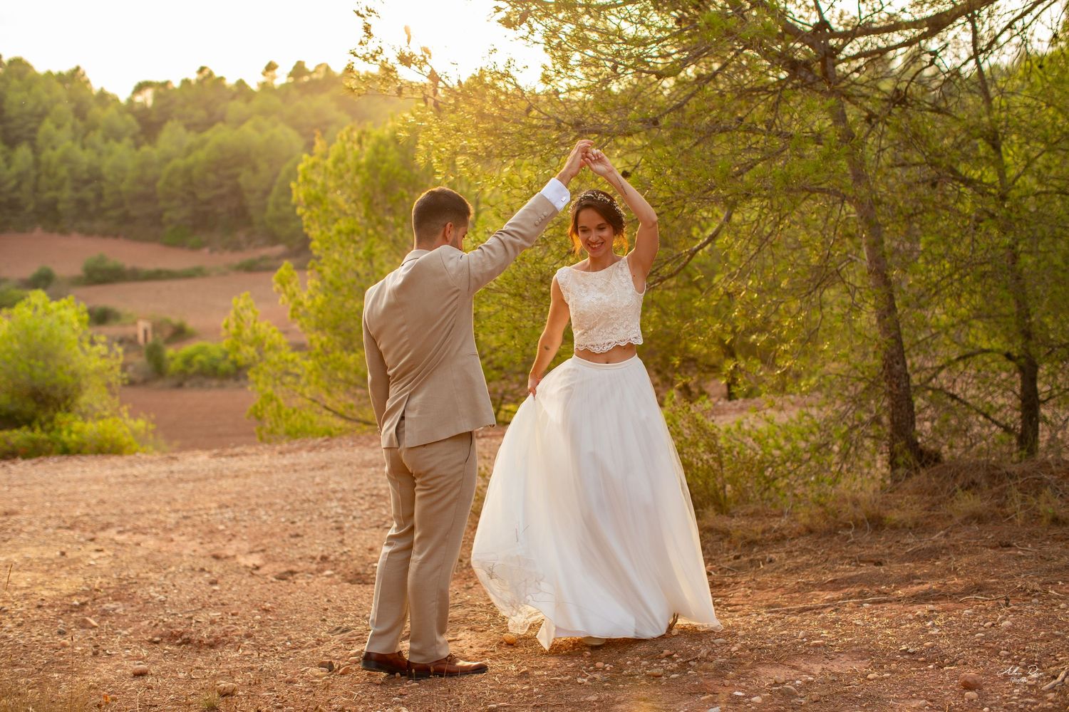 Groom twirling his bride in a joyful dance among sunlit trees at golden hour.