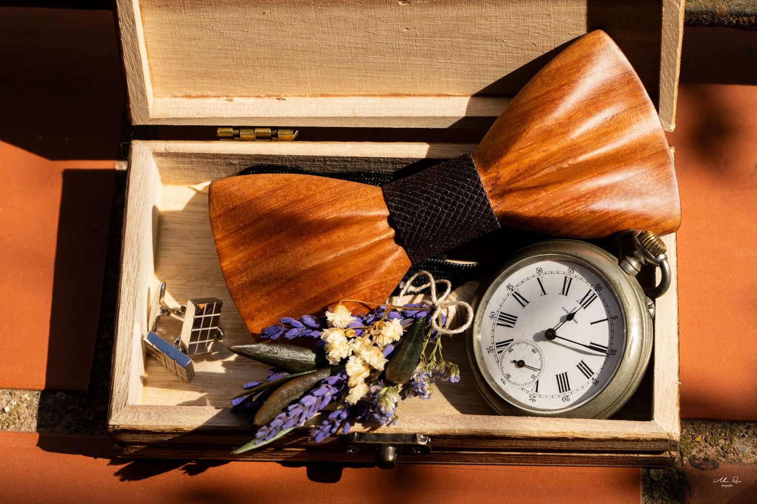Wooden bow tie and pocket watch displayed in a rustic wooden box with dried lavender.