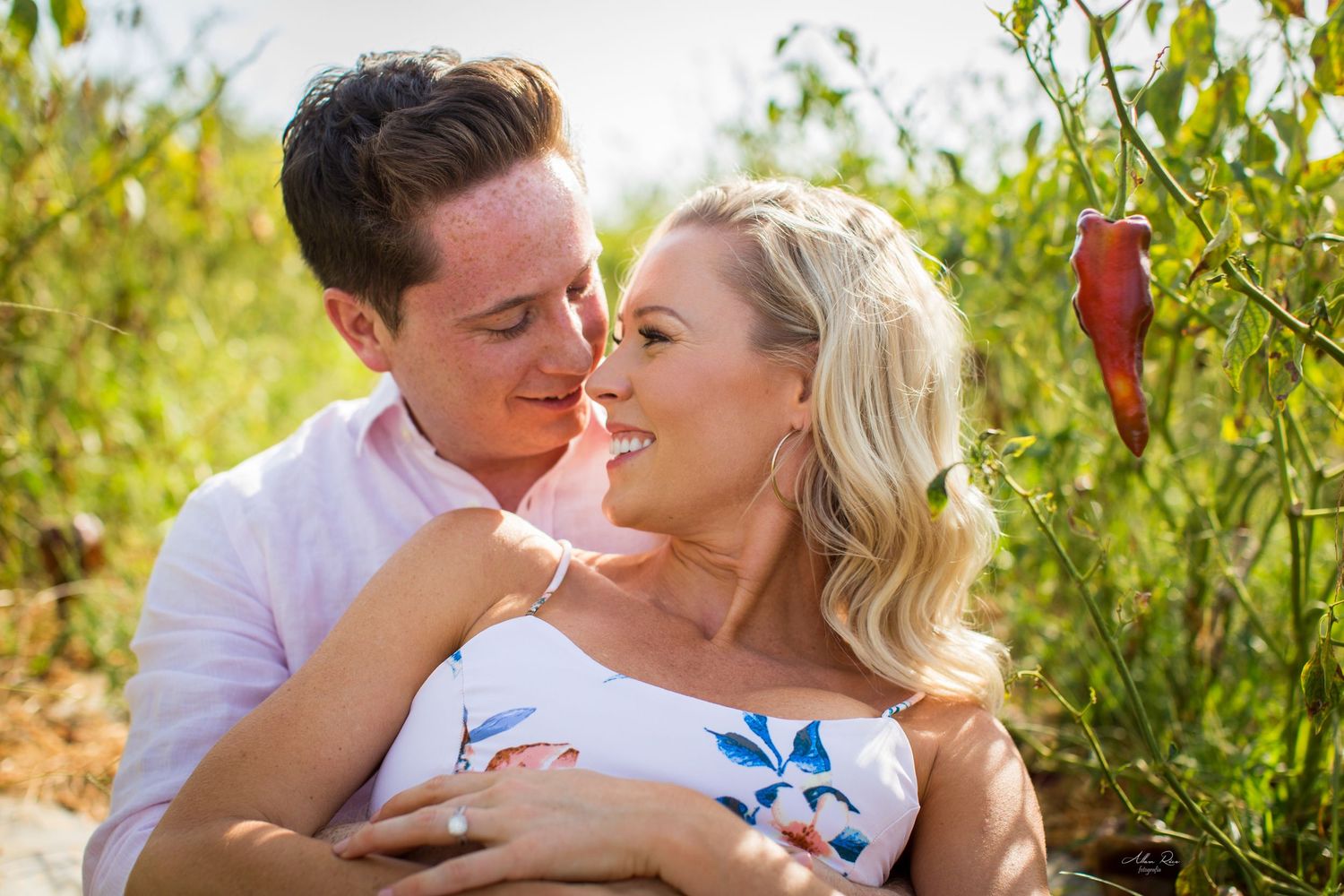 Loving couple embracing and smiling at each other surrounded by green foliage in natural setting.