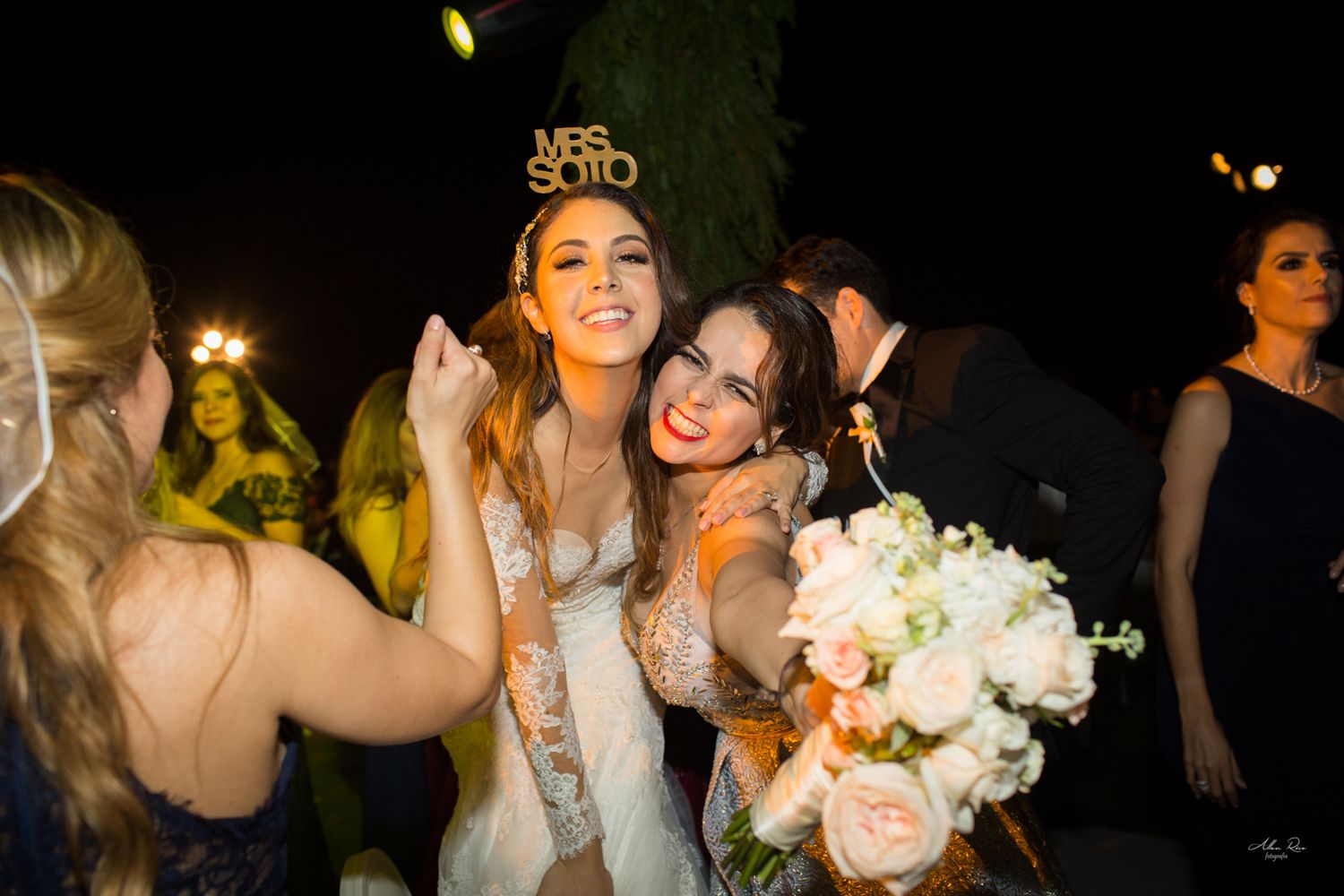 Bride wearing Mrs Soto crown hugging friend at wedding reception.