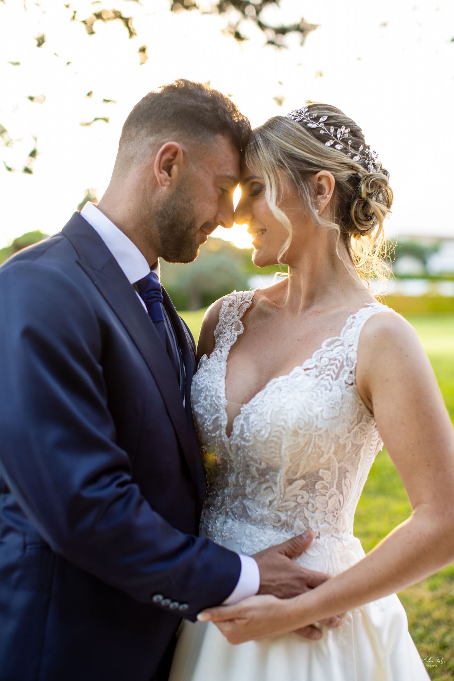 Bride and groom touch foreheads romantically at golden sunset in an outdoor wedding portrait.