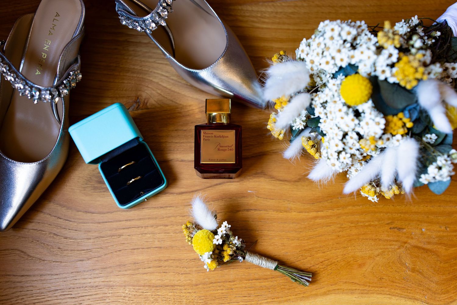 Wedding flat lay with silver heels, Tiffany ring box, gold rings, perfume, and floral bouquet.