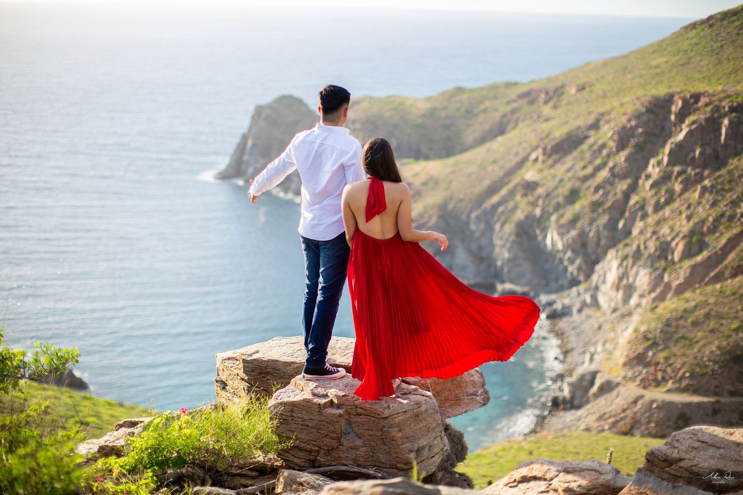 Couple standing on rocky cliff overlooking stunning blue coastal scenery.