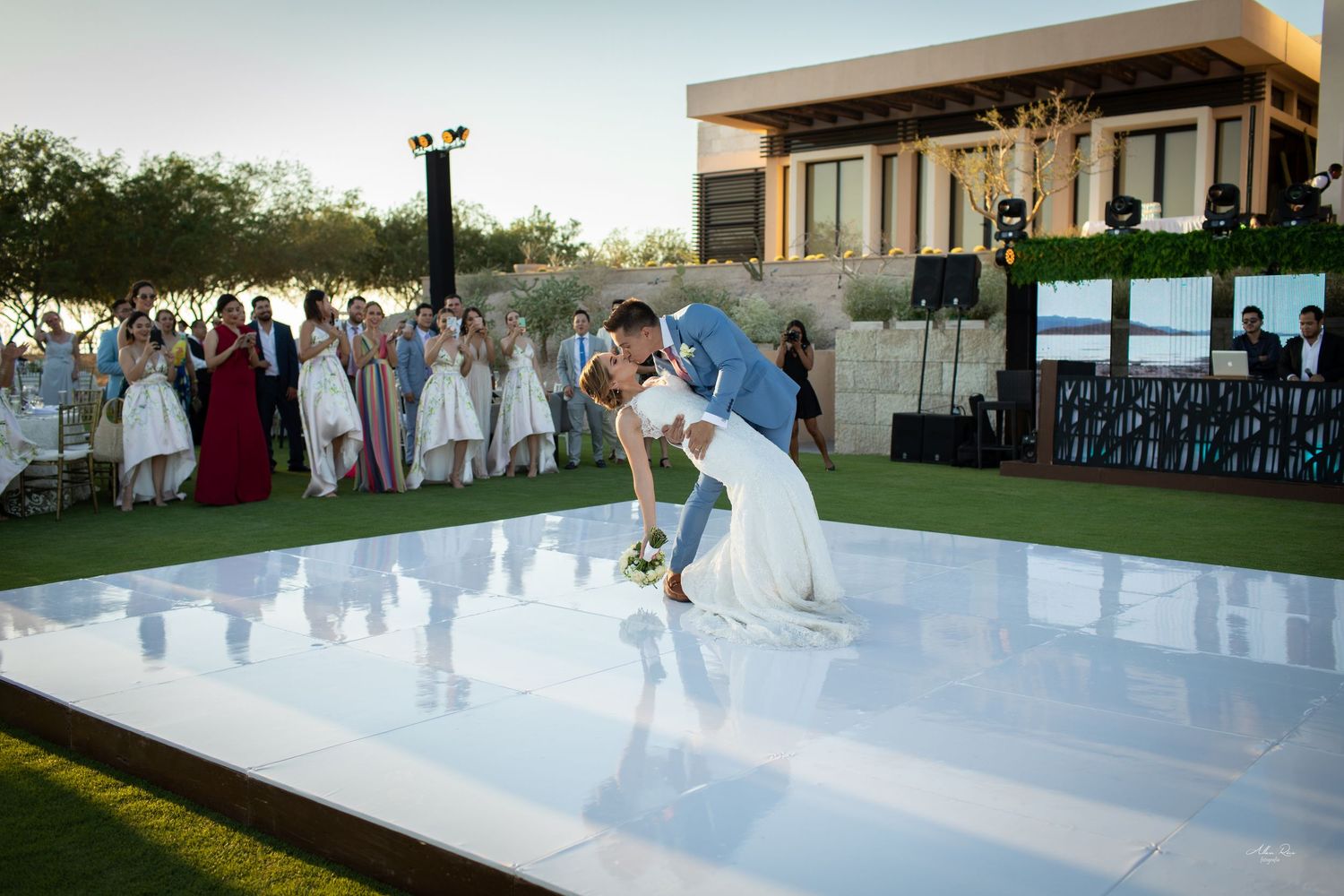 Bride and groom sharing a dramatic dip kiss on a white dance floor at outdoor wedding reception.