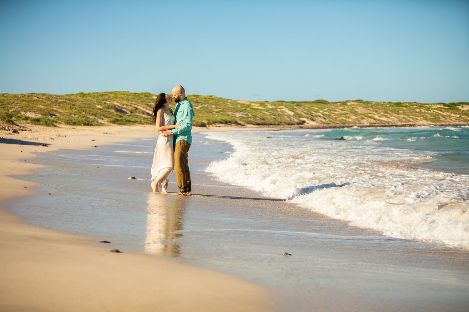 Romantic couple embracing at the shoreline on a sunny beach.