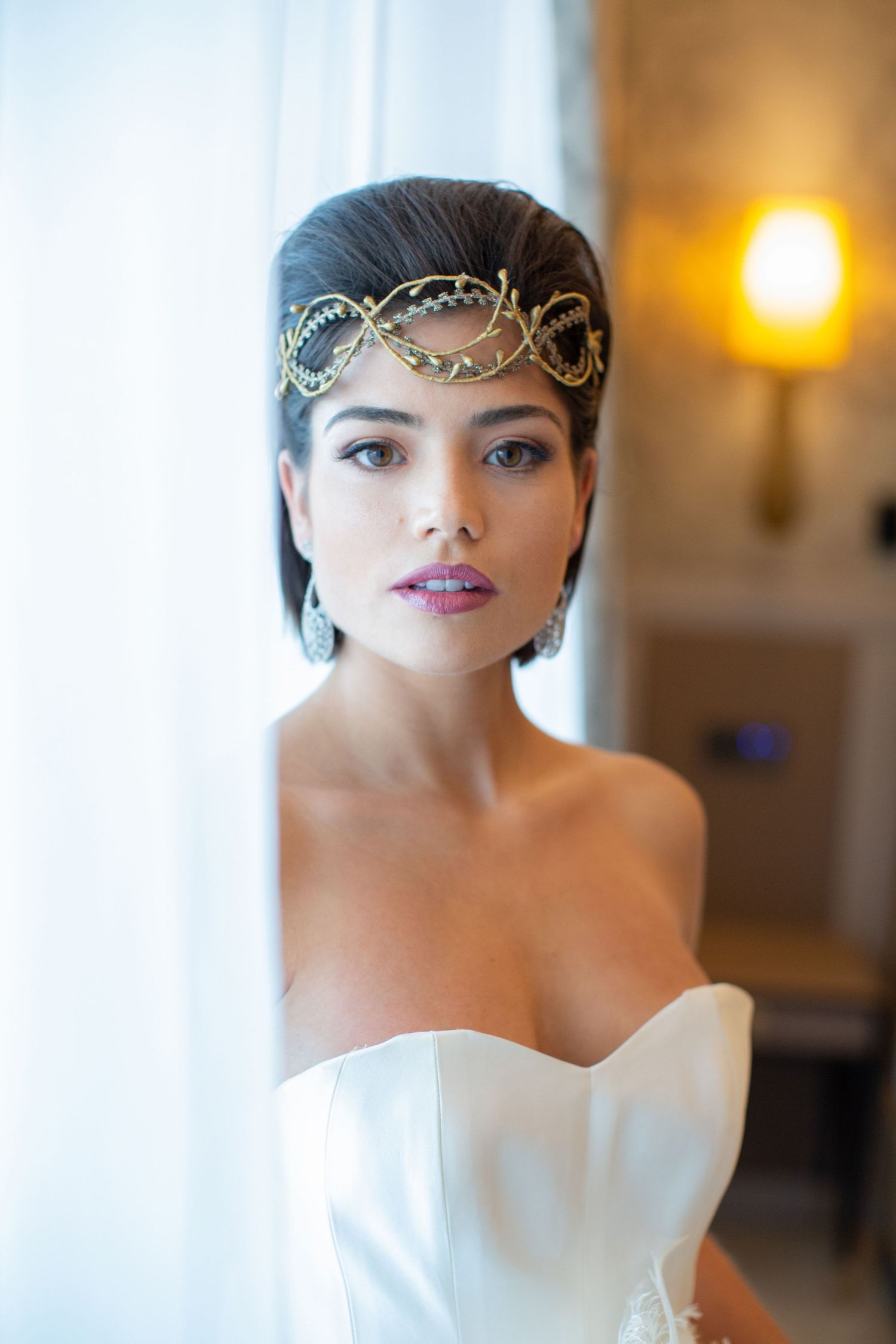 Close-up portrait of a bride wearing an ornate gold headpiece and strapless white gown with dramatic makeup.