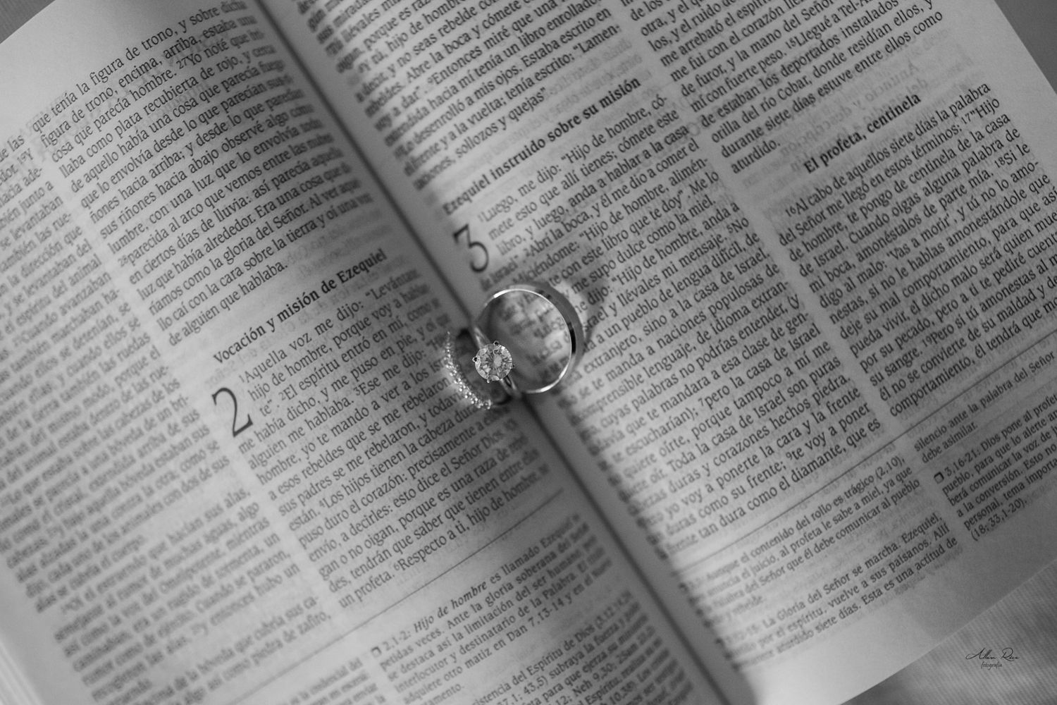 Wedding rings resting on an open Bible in a black and white photo.