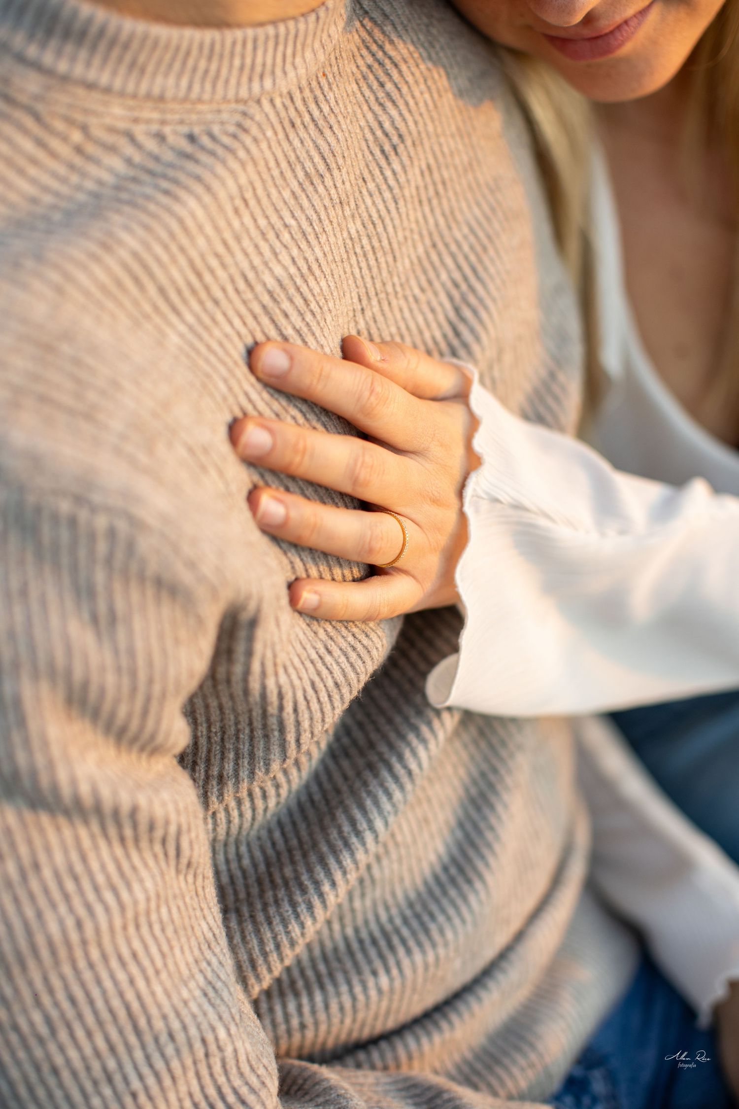 Close-up of a couple holding hands, woman wearing a gold ring, man in a beige knit sweater.
