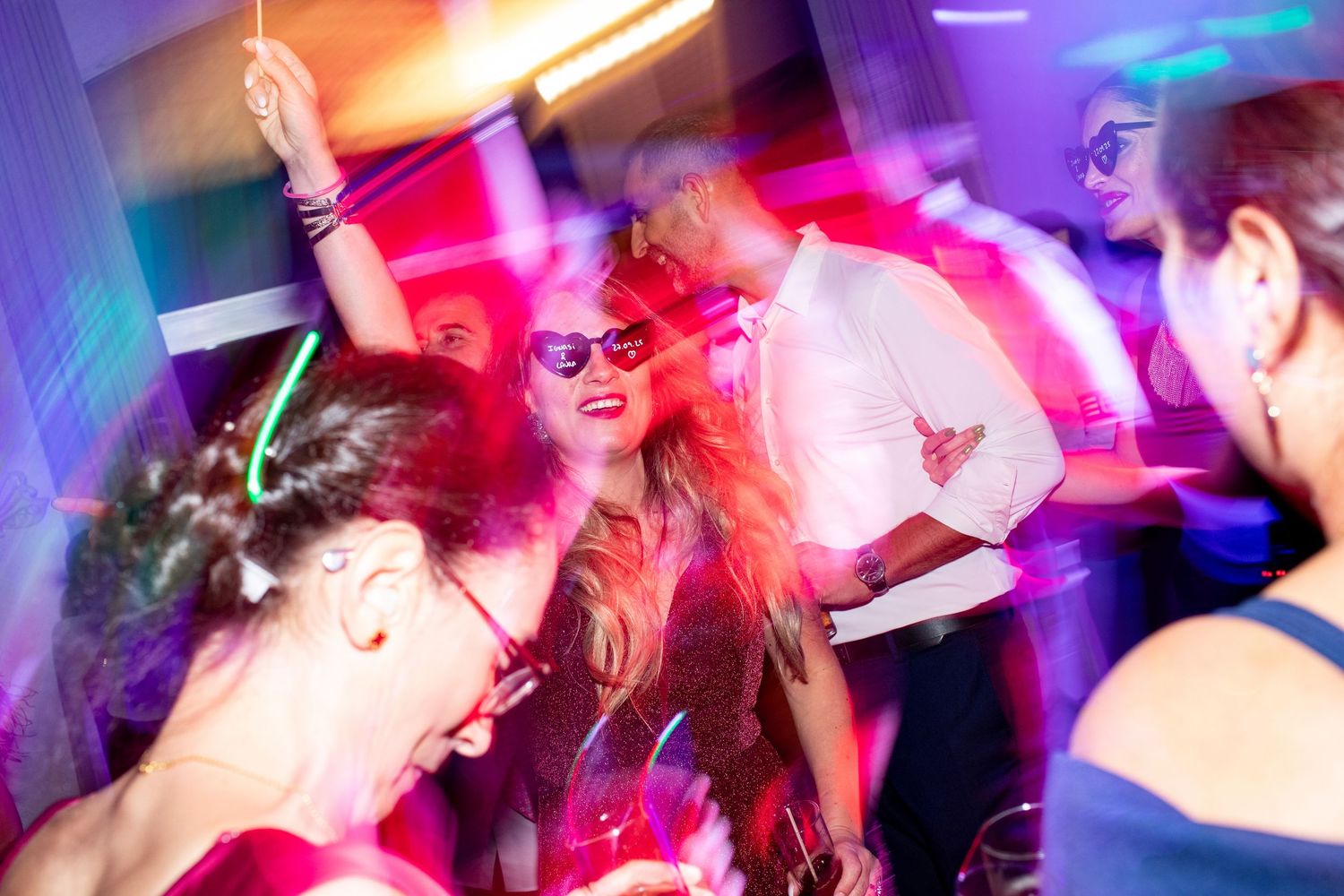 Guests dancing joyfully under vibrant purple and pink lights at wedding reception.