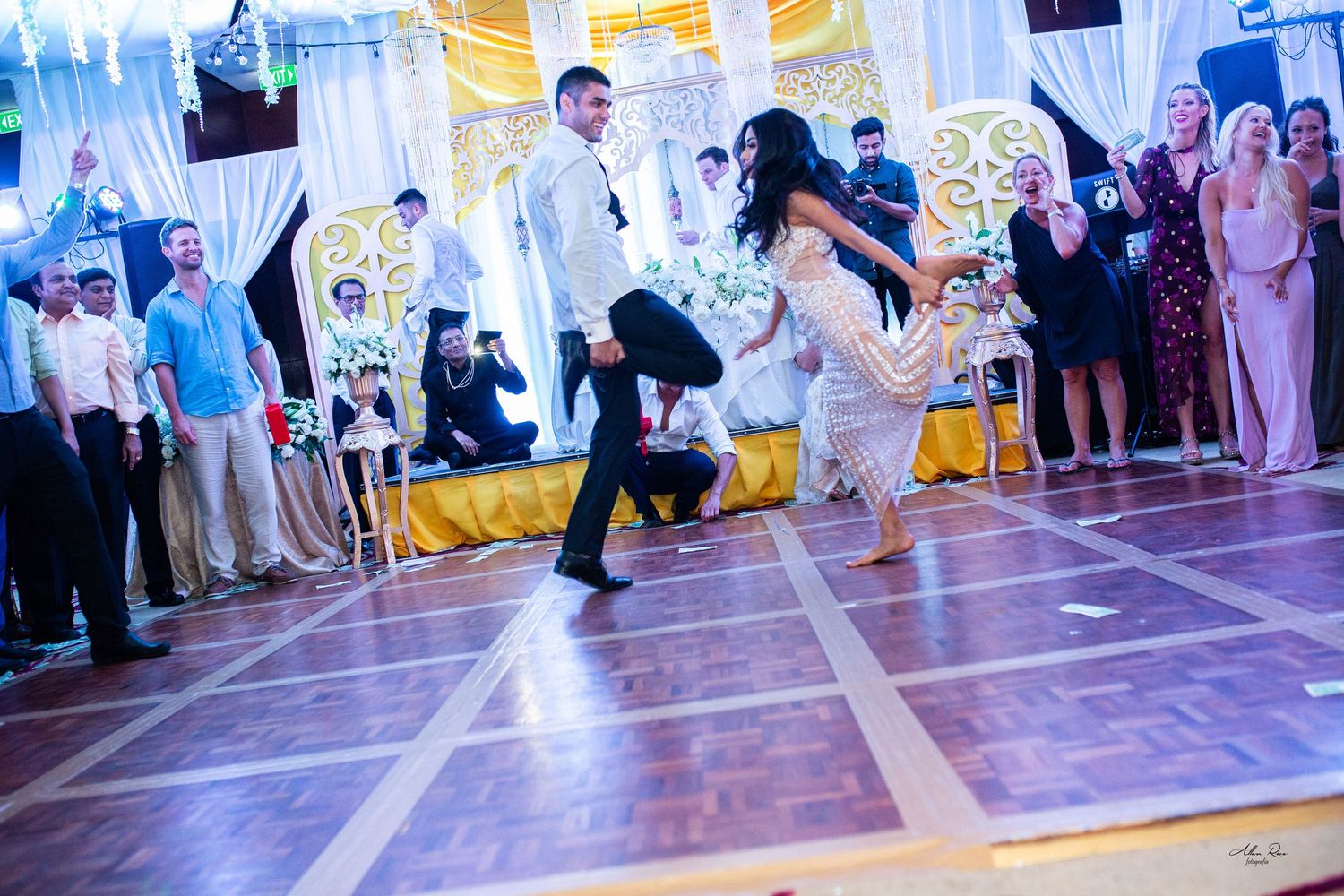 Bride and groom performing an energetic first dance on a wooden ballroom floor at their wedding reception.
