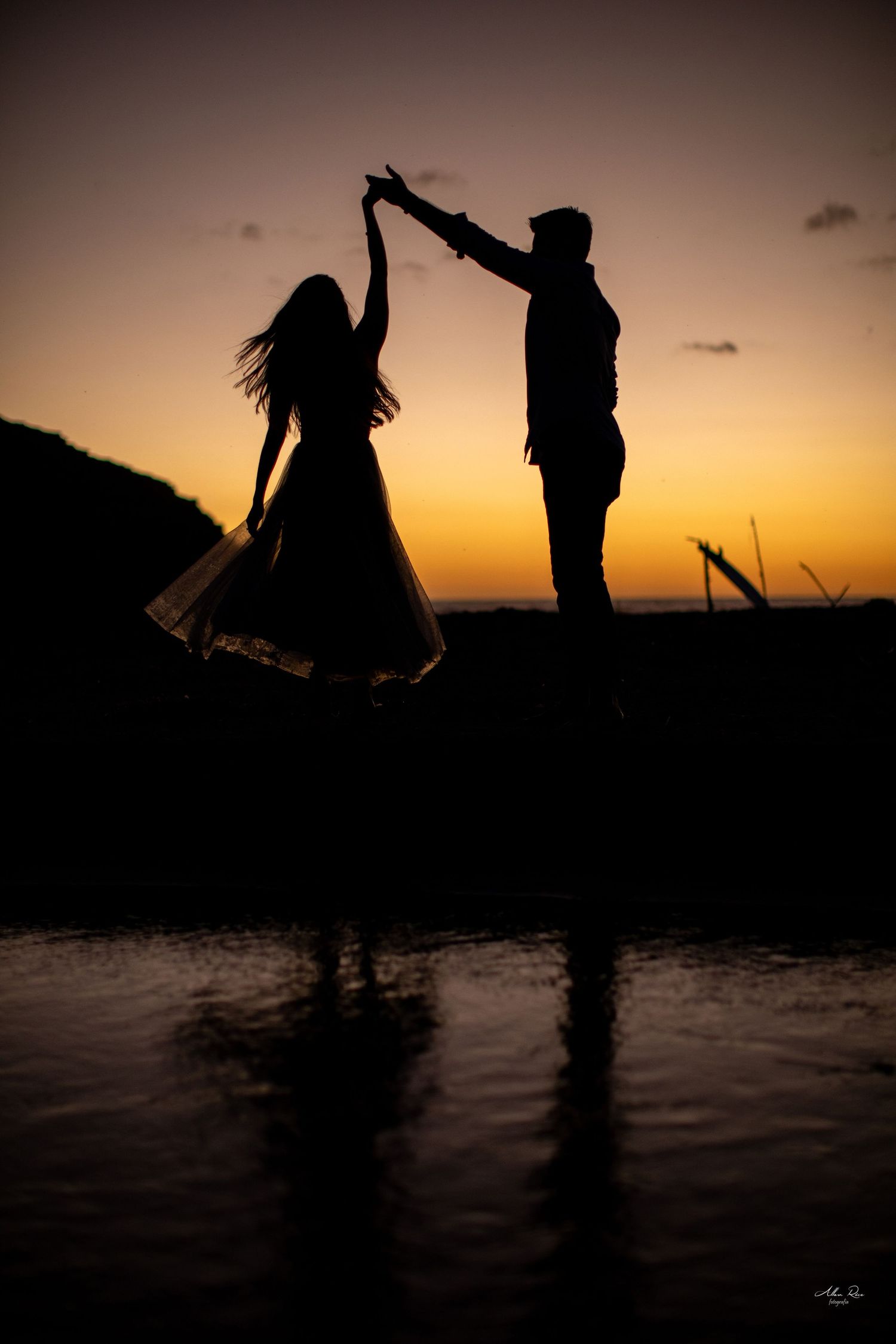 Romantic silhouette of dancing couple against vibrant orange sunset.