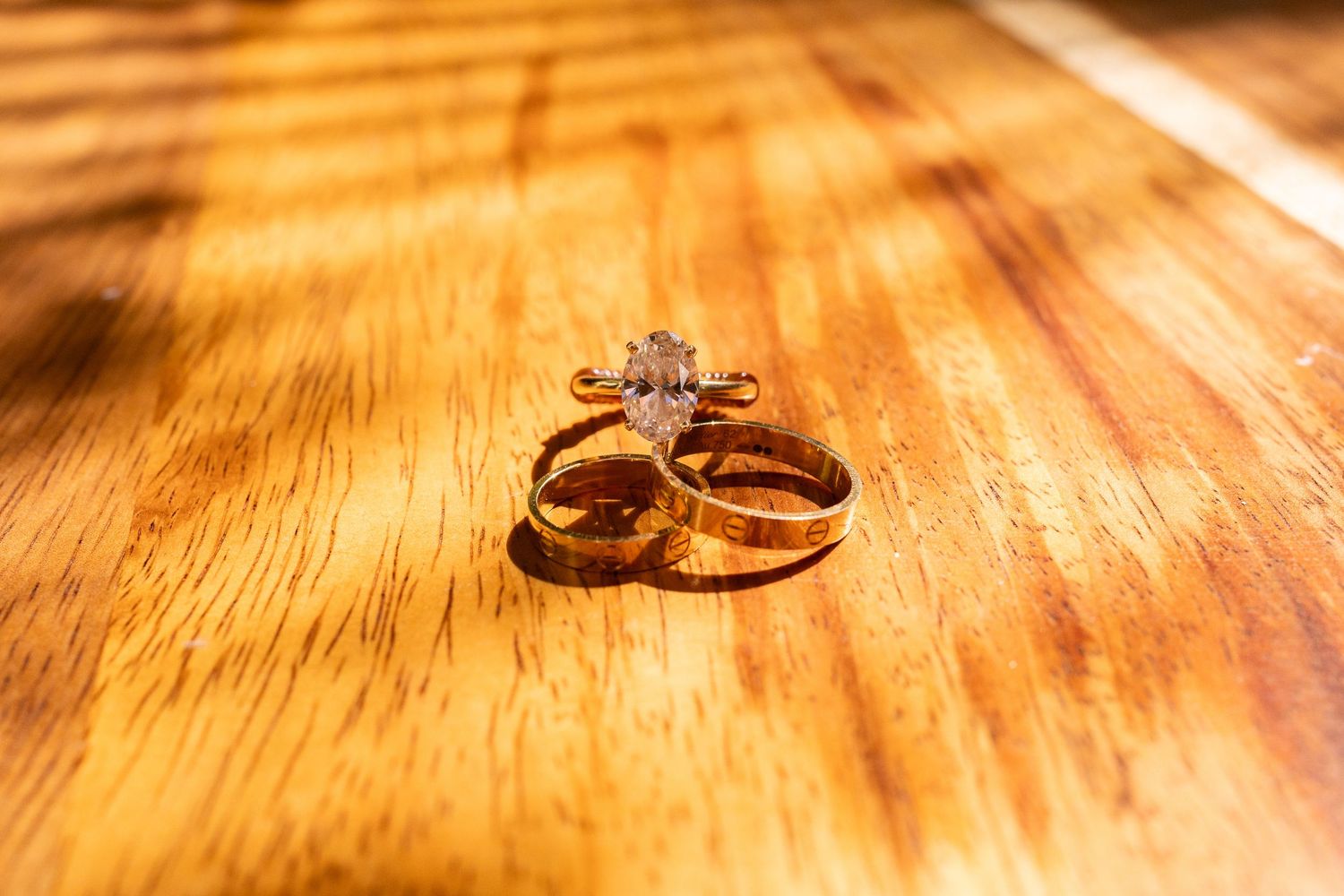Gold wedding rings with diamond engagement ring on wooden surface.
