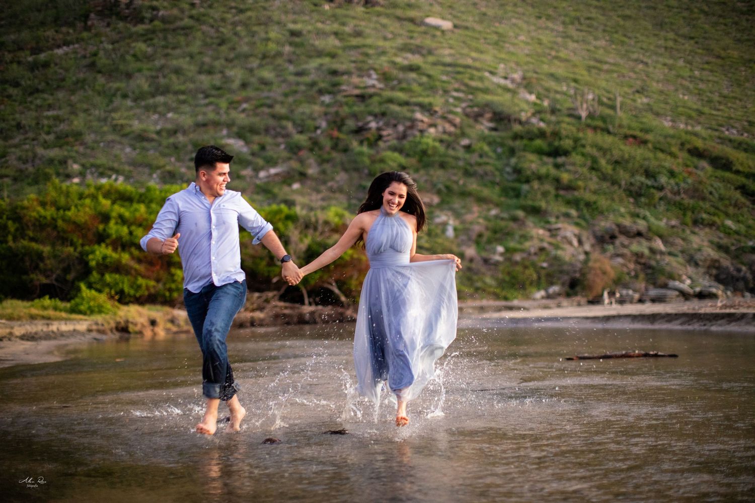 Couple laughing and splashing through shallow beach water together.