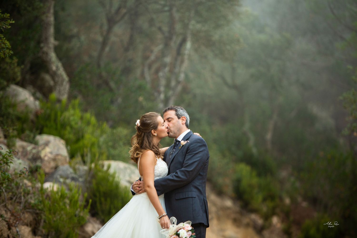 Wedding couple shares romantic moment in foggy woodland with lush greenery backdrop.