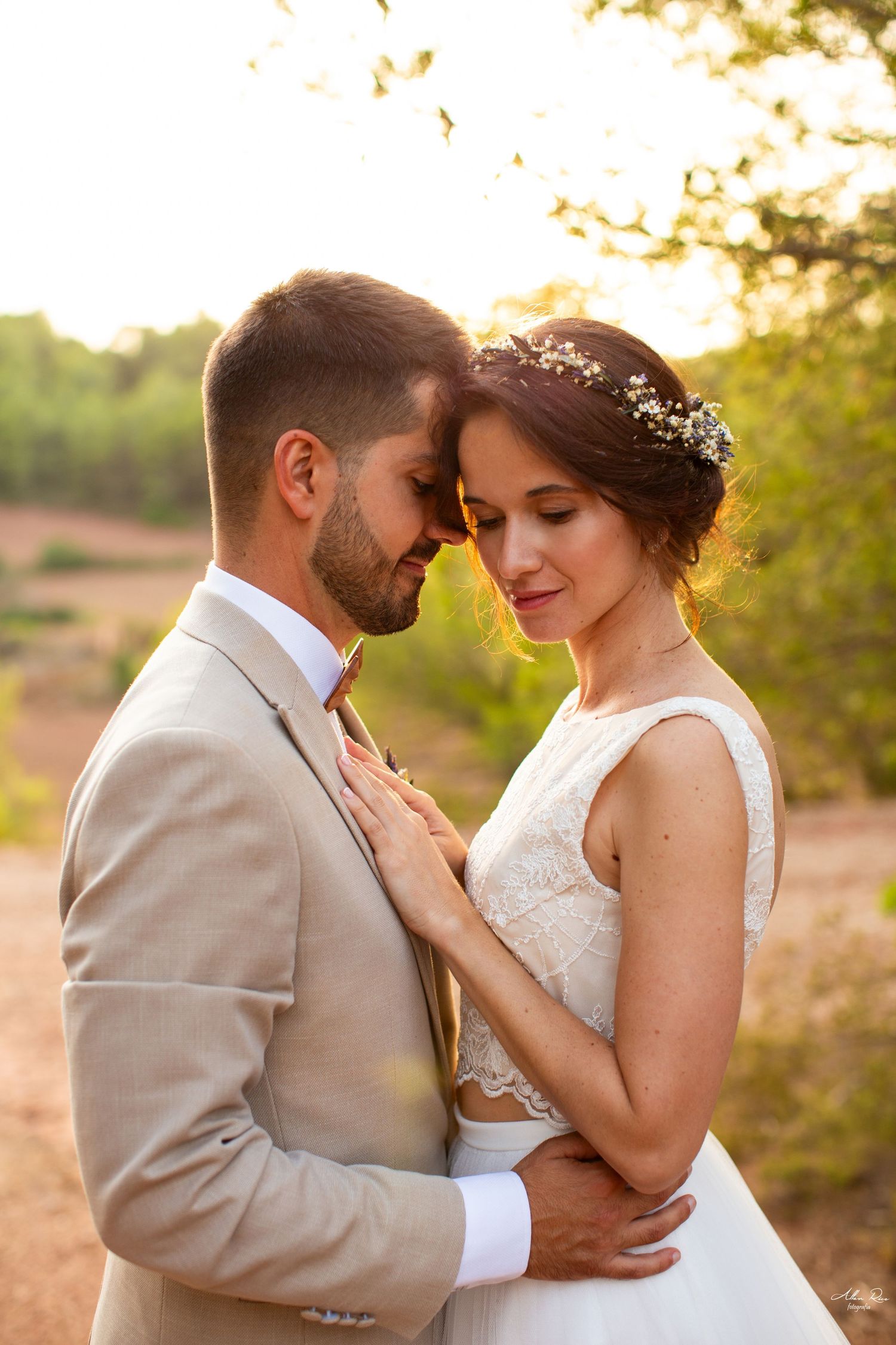 Bride and groom touching foreheads tenderly in a warm golden sunset outdoor setting.