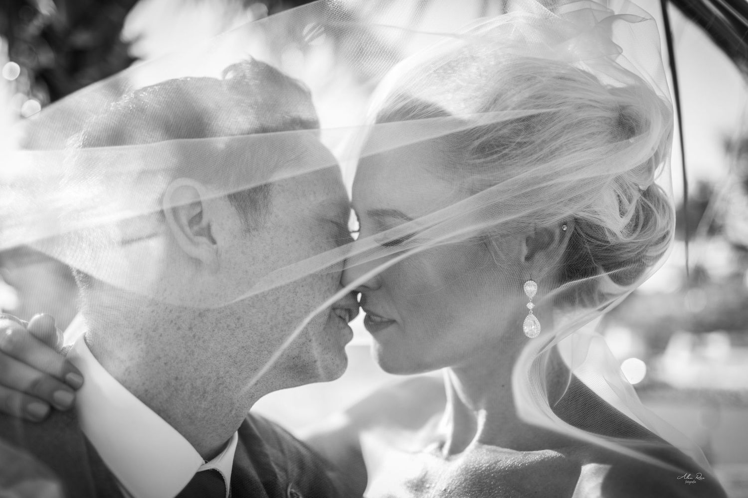 Romantic black and white photo of bride and groom almost kissing under flowing wedding veil.