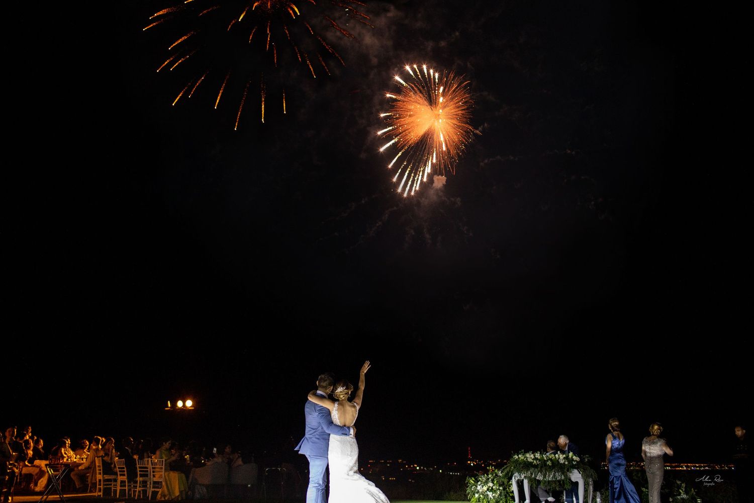 Bride and groom watching colorful fireworks display light up the night sky at wedding reception.