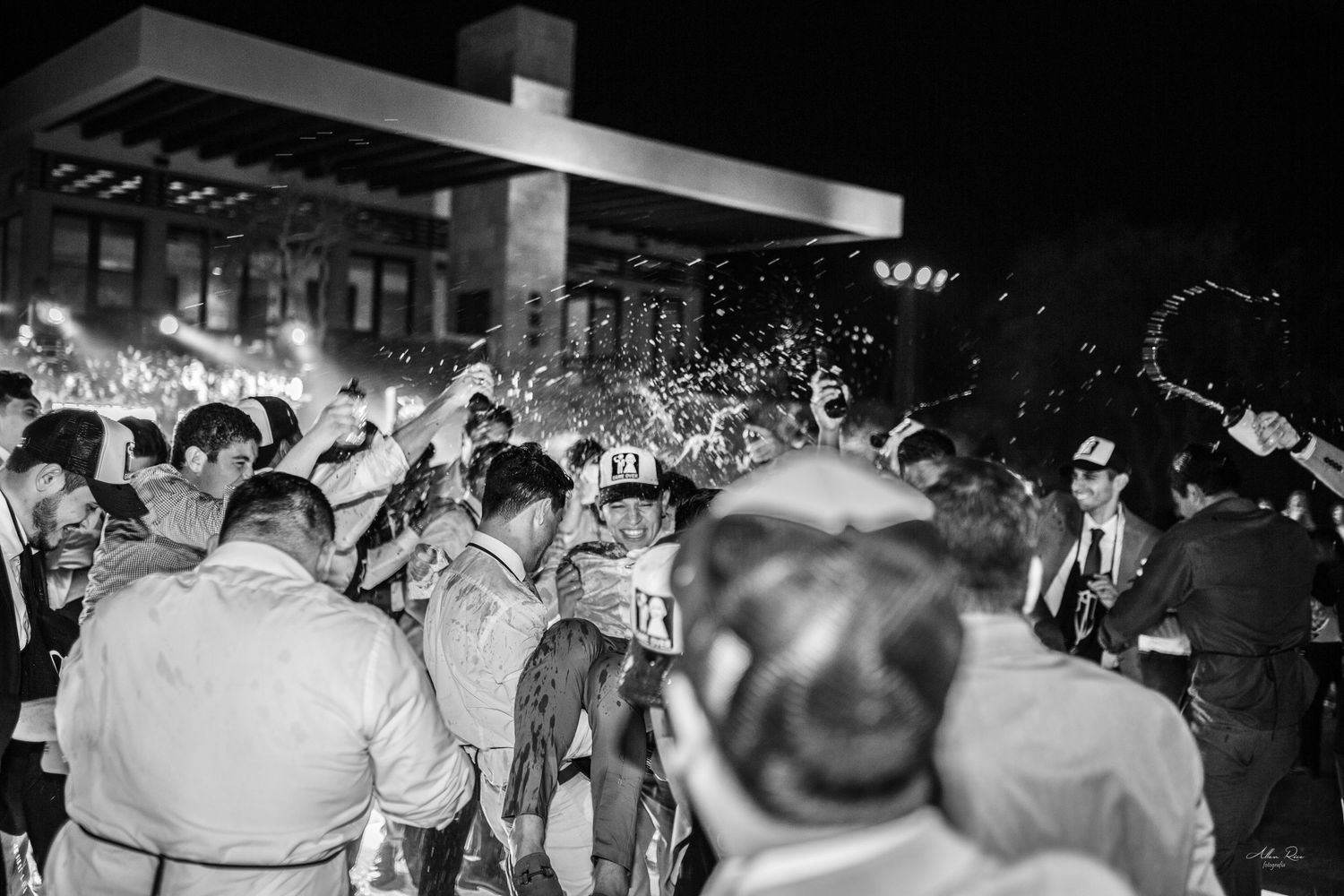 Black and white photo of wedding guests celebrating with champagne spray at night reception.