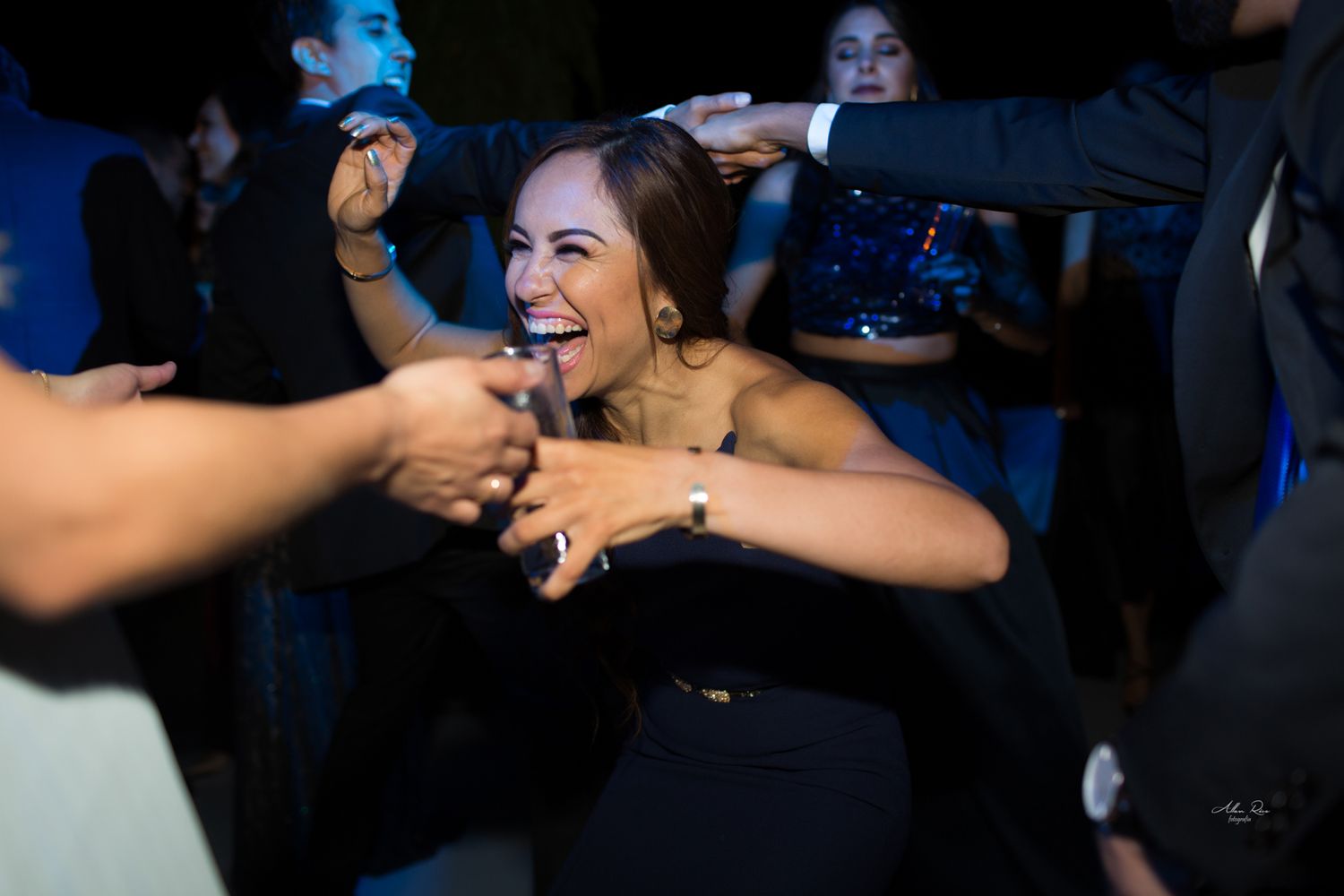 Woman laughing joyfully while dancing with guests at energetic nighttime outdoor wedding reception party.