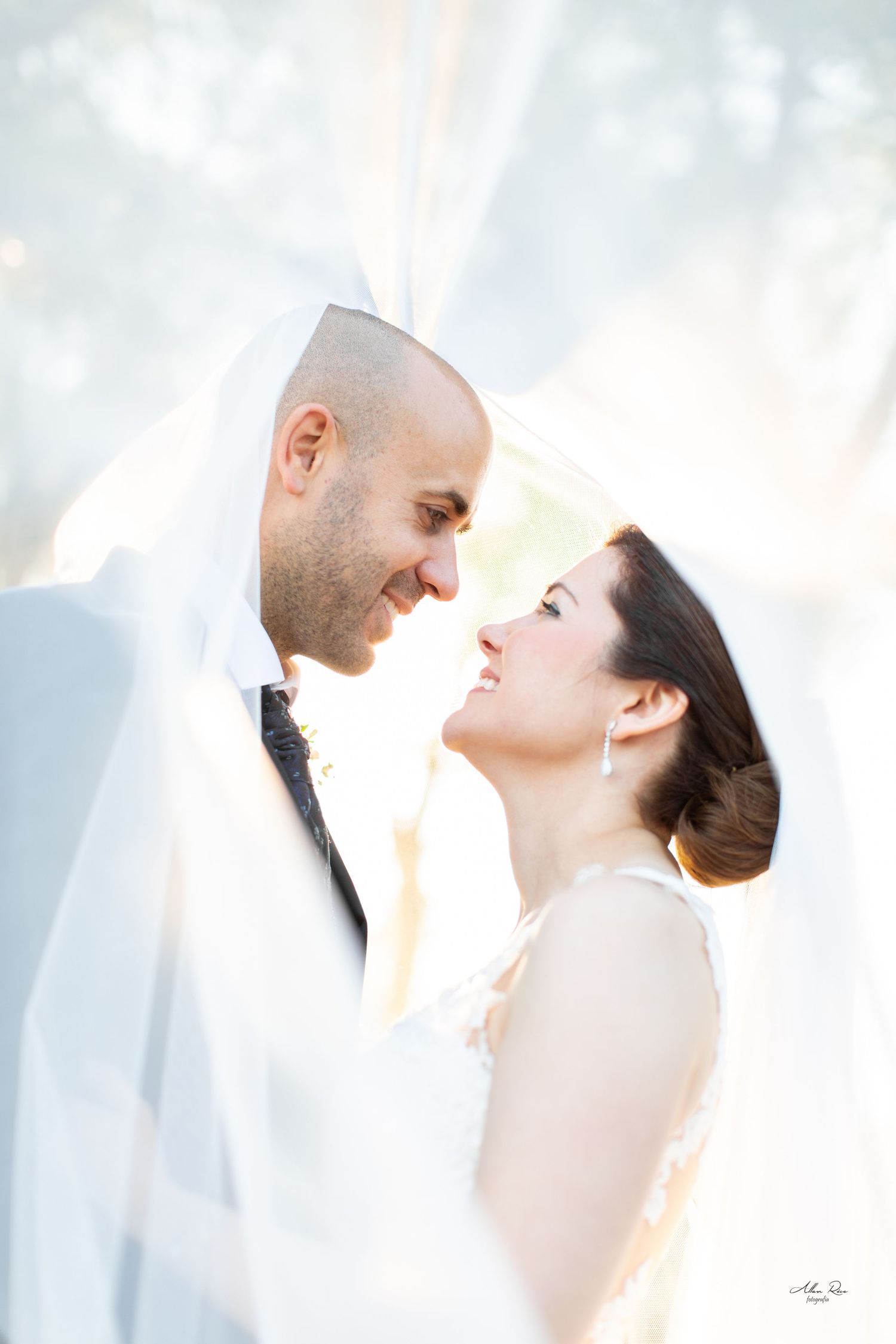 Romantic bride and groom sharing an intimate moment under a flowing white veil outdoors.