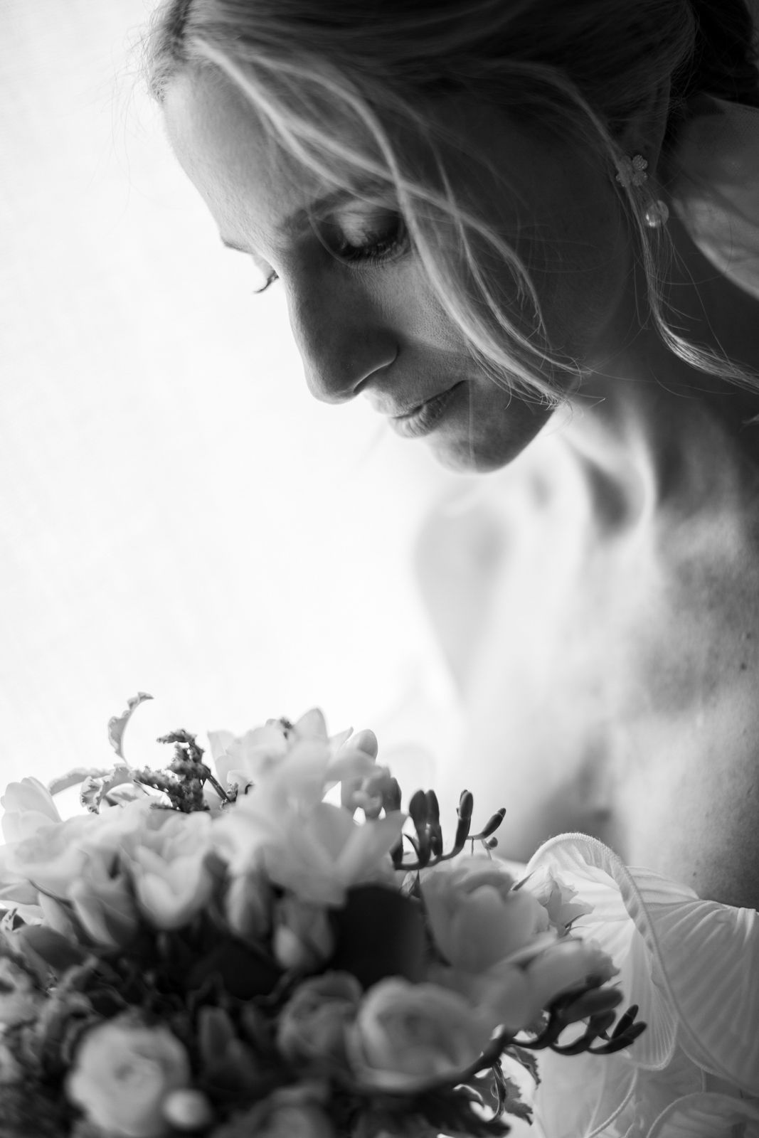 Black and white portrait of a smiling bride looking down at her bouquet of delicate white flowers.