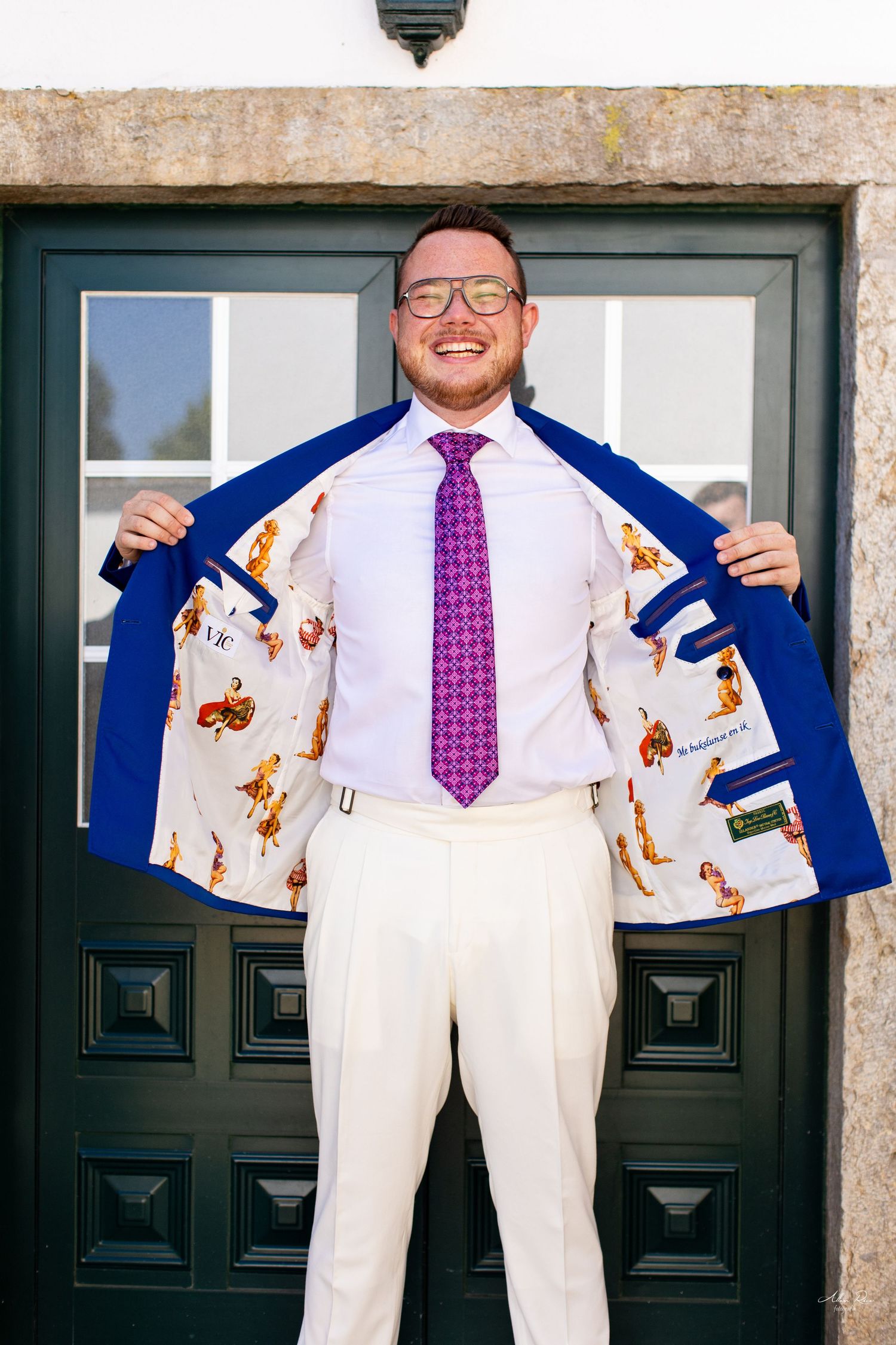 Smiling groom in blue suit showing decorative lining outside church doors.