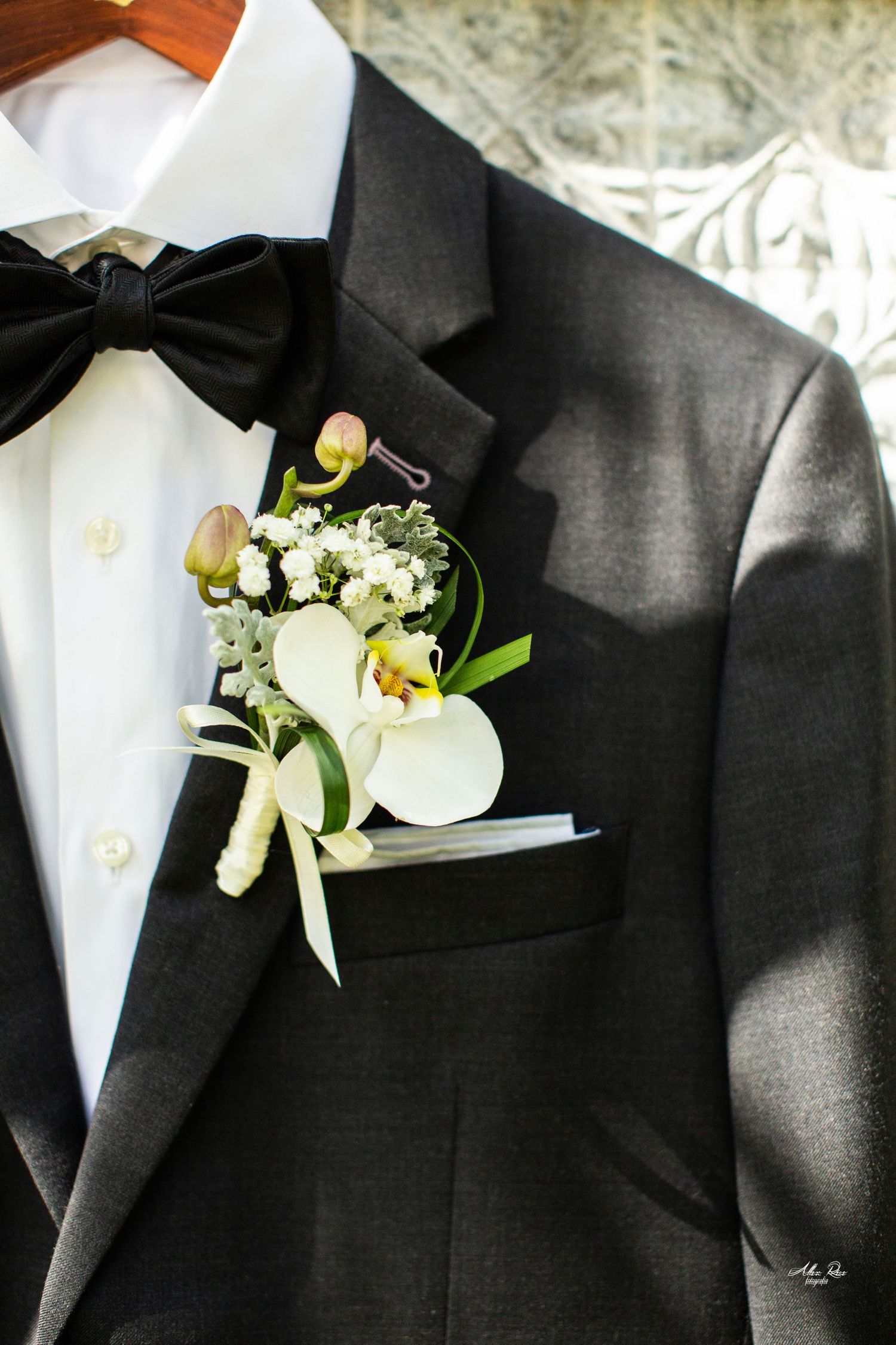 Close-up of groom's black tuxedo lapel featuring white orchid boutonniere with black bow tie.