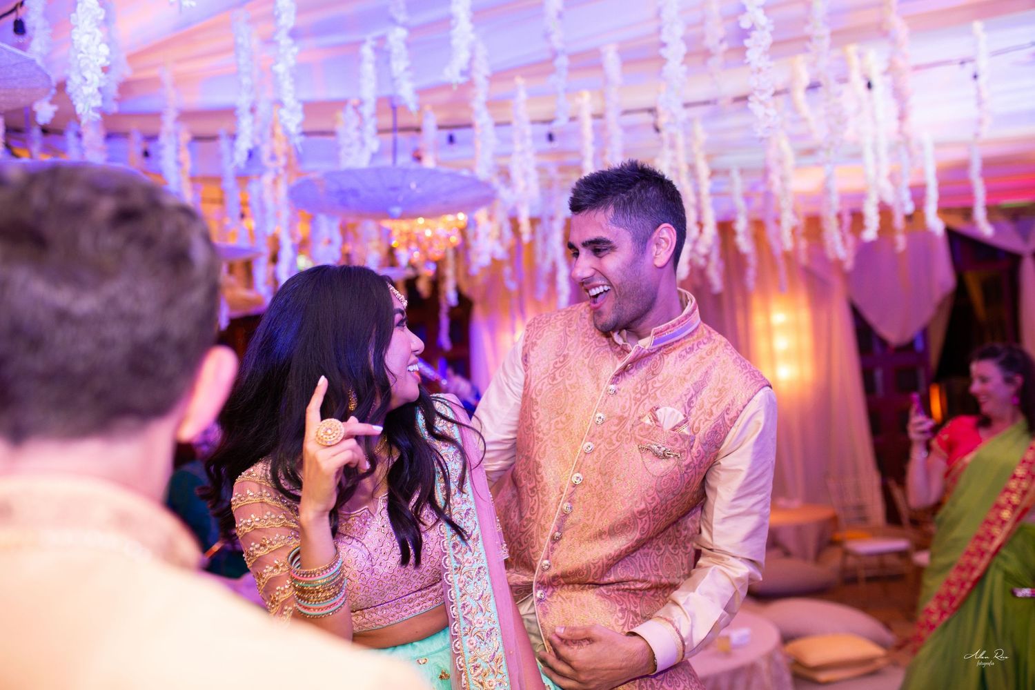 Indian couple laughing and dancing joyfully at a vibrant wedding reception celebration.