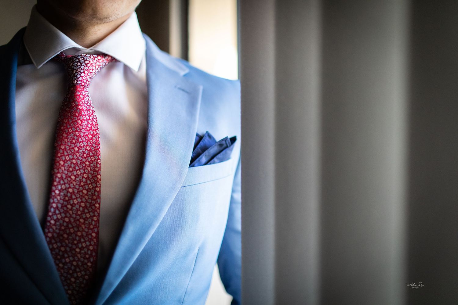 Close-up detail of groom's light blue suit with pink patterned tie and navy pocket square.