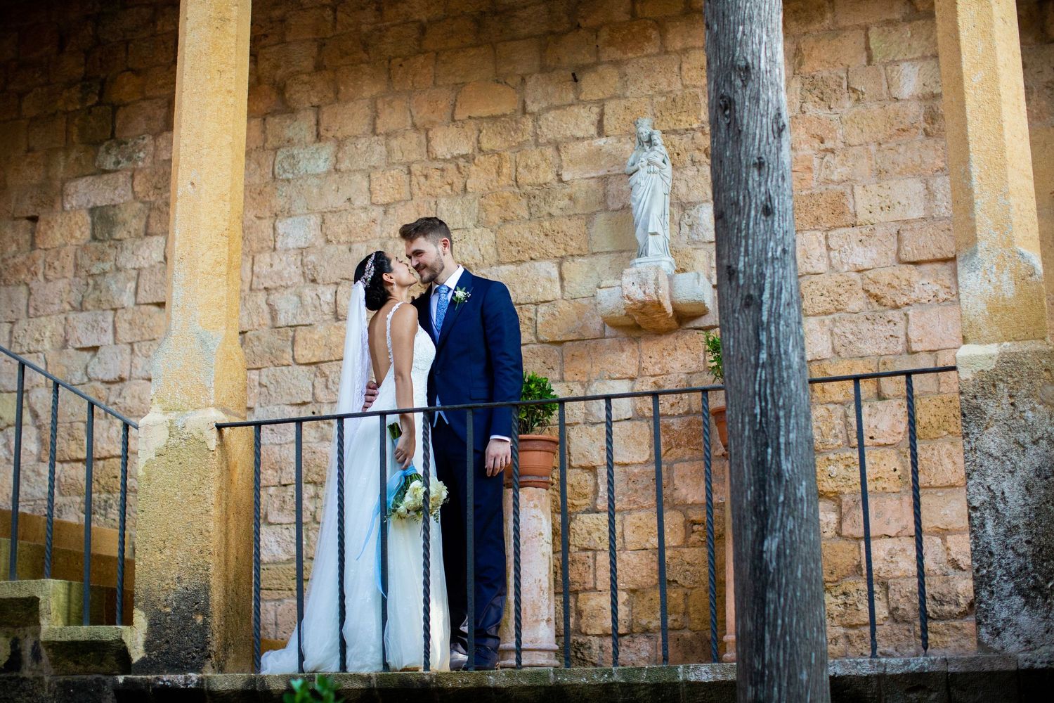 Wedding couple sharing a romantic kiss on a historic stone building balcony.