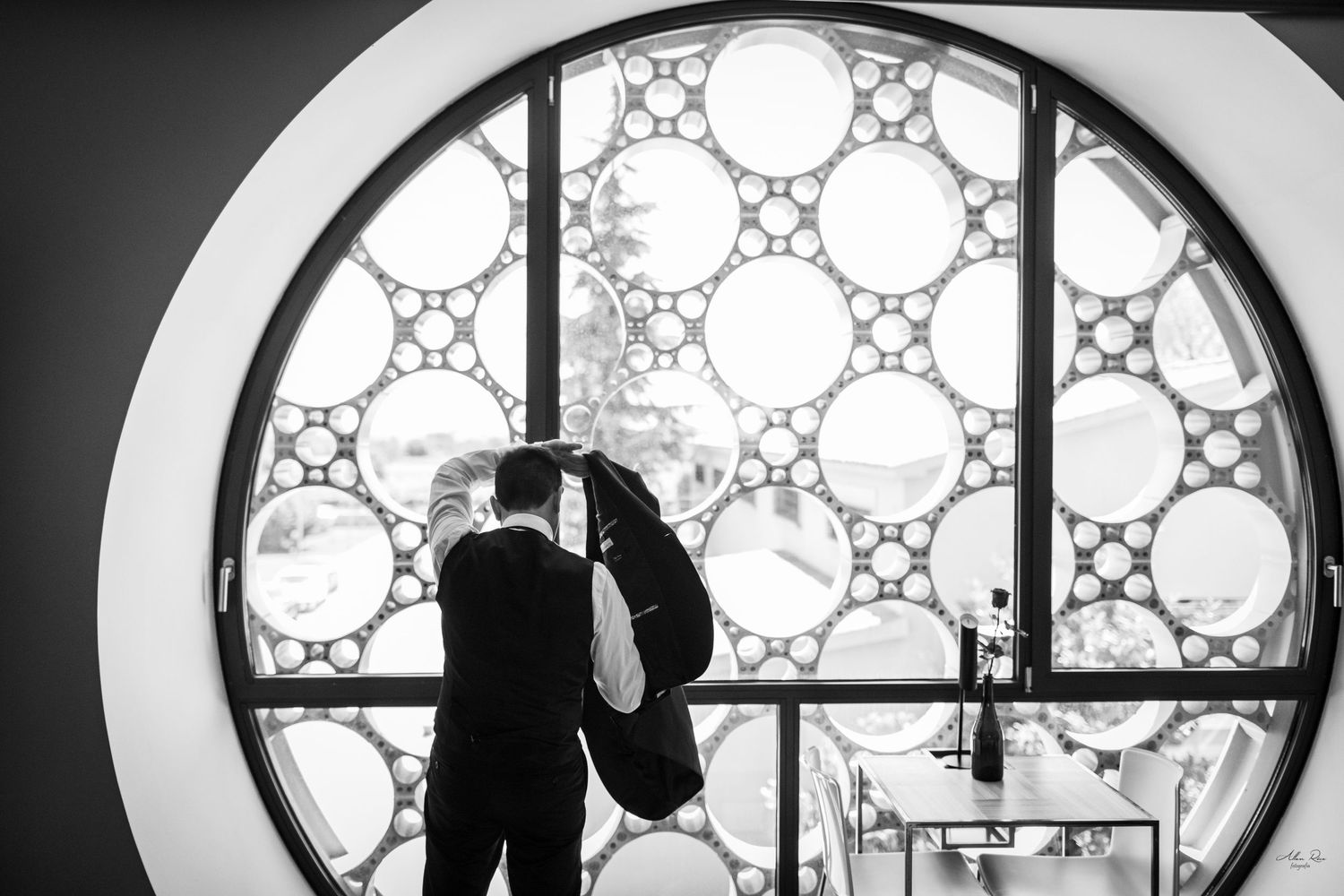 Groom standing before a large circular decorative window in black and white photo.