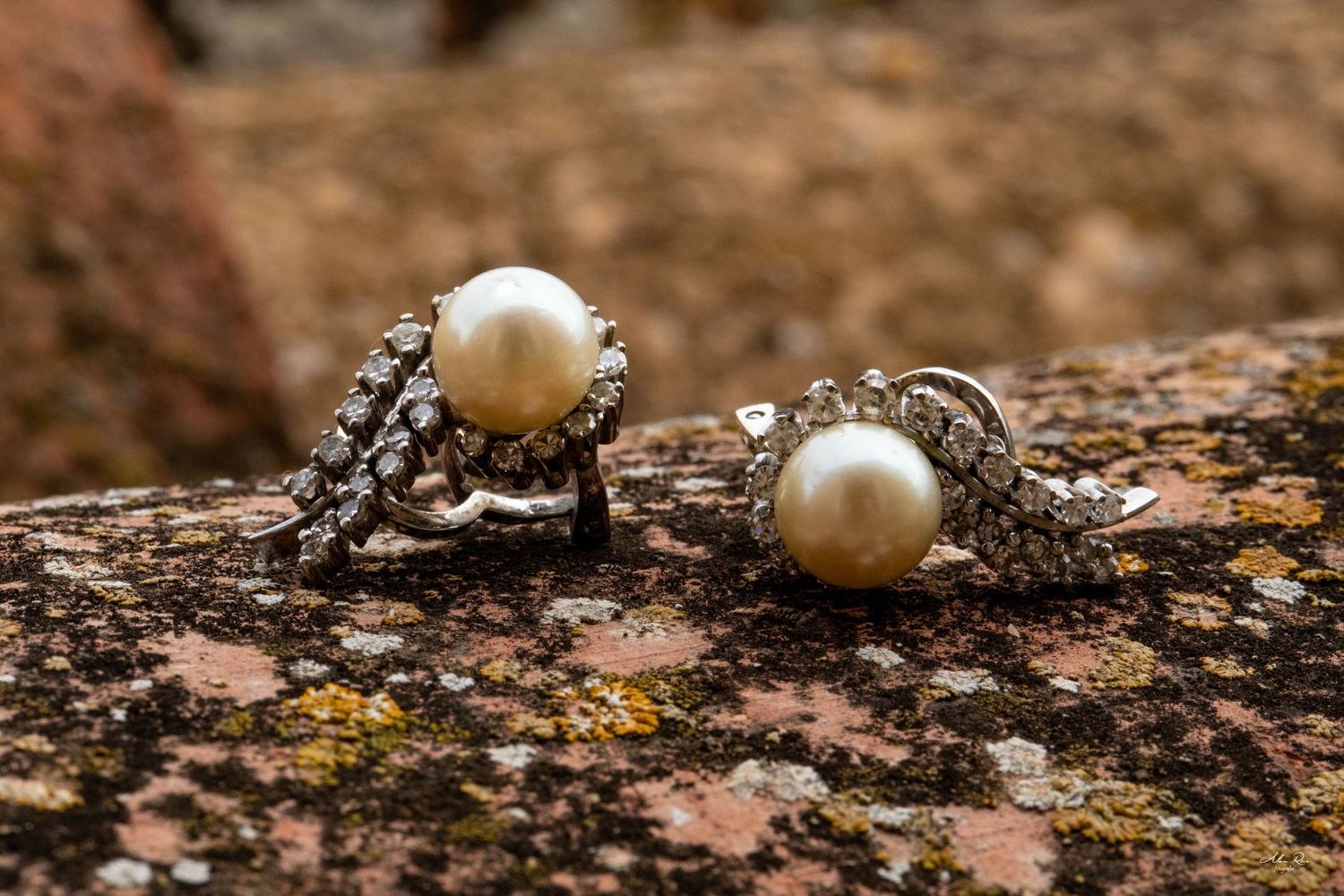Elegant pearl and diamond earrings displayed on a textured granite rock surface.
