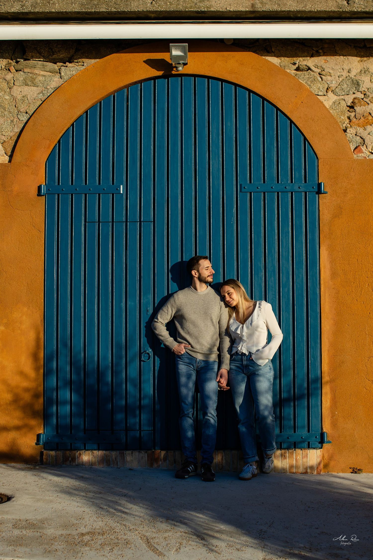 Couple standing together in front of a vibrant blue arched door set in an orange wall.