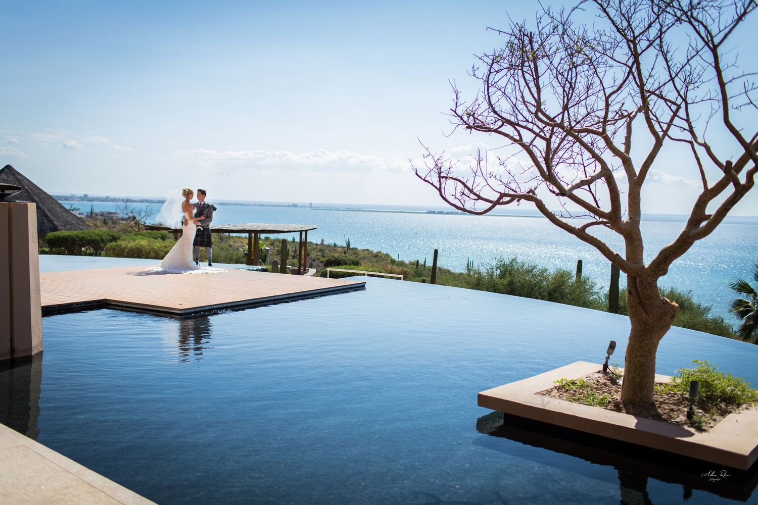Bride and groom embracing beside infinity pool overlooking stunning ocean at sunset.